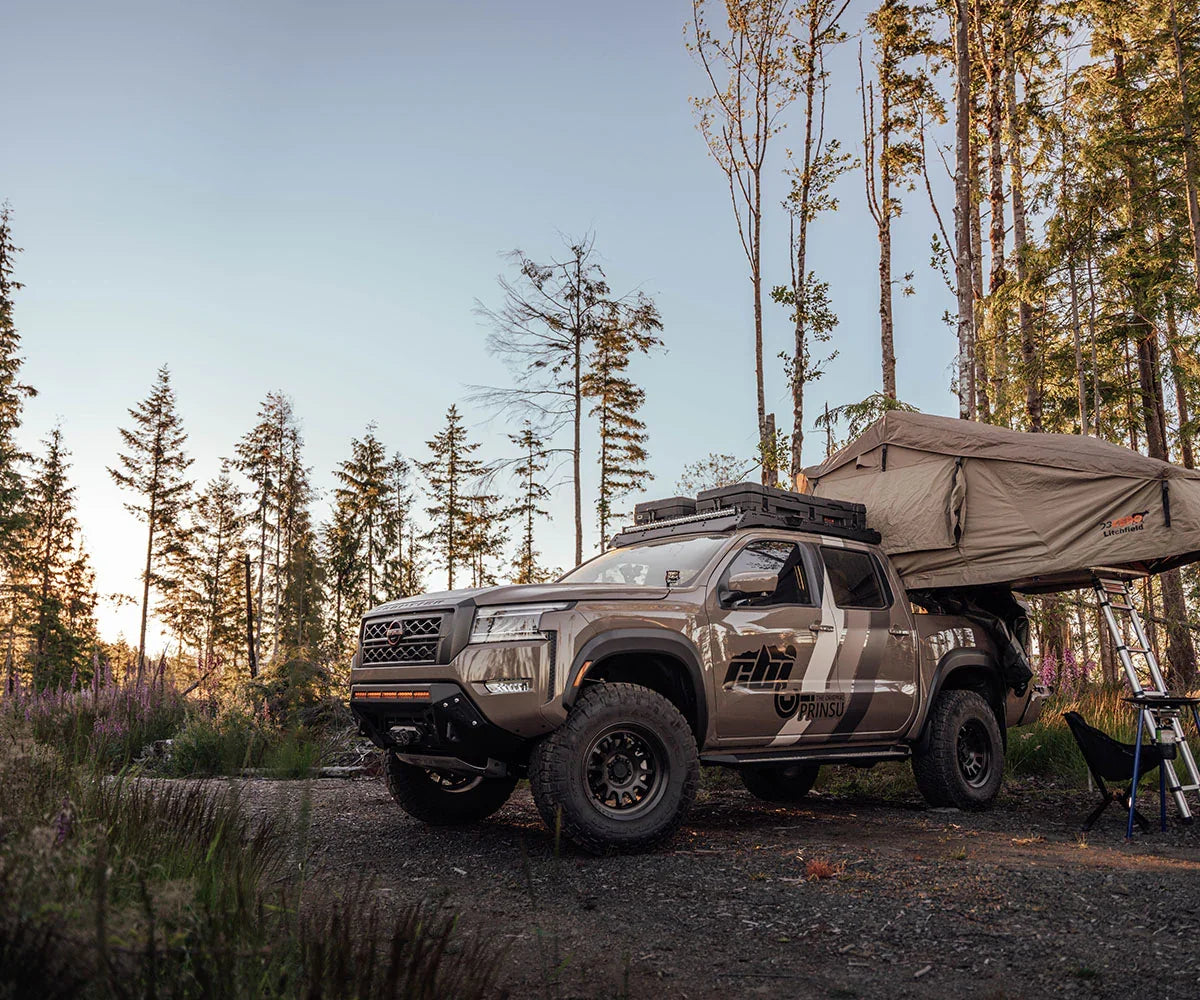 Nissan Frontier overland truck with rooftop tent and off-road gear in a forest campsite