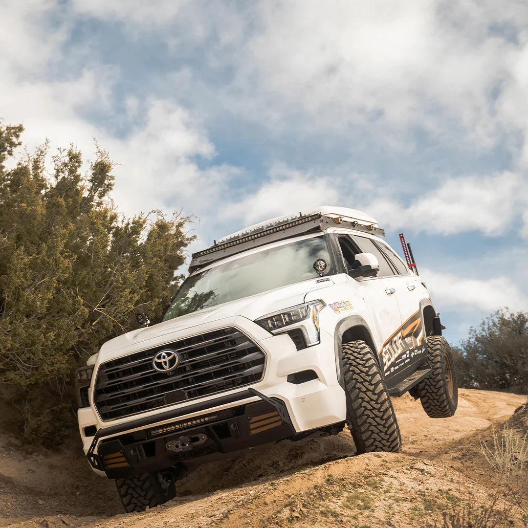 White overland-built Toyota Sequoia off-roading on a dirt trail with rugged gear