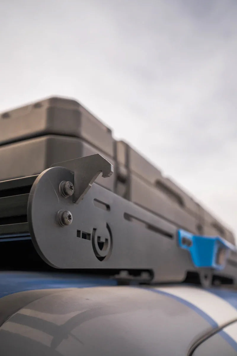 Close-up of a metal bottle opener mounted on a roof rack with gear storage boxes, overland vehicle accessory.