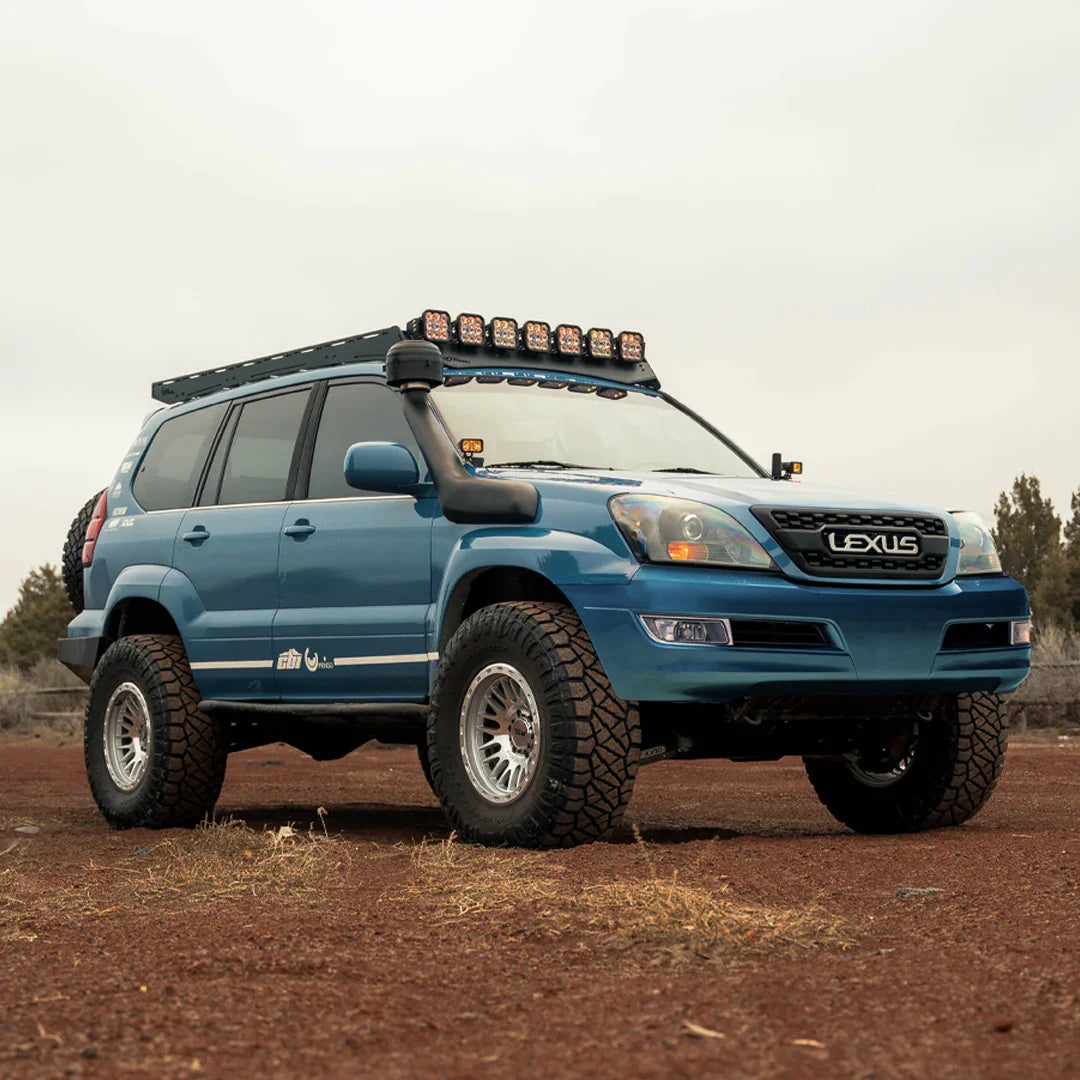 Lifted blue Lexus GX 470 SUV with off-road tires, roof rack, and LED light bar in outdoor setting