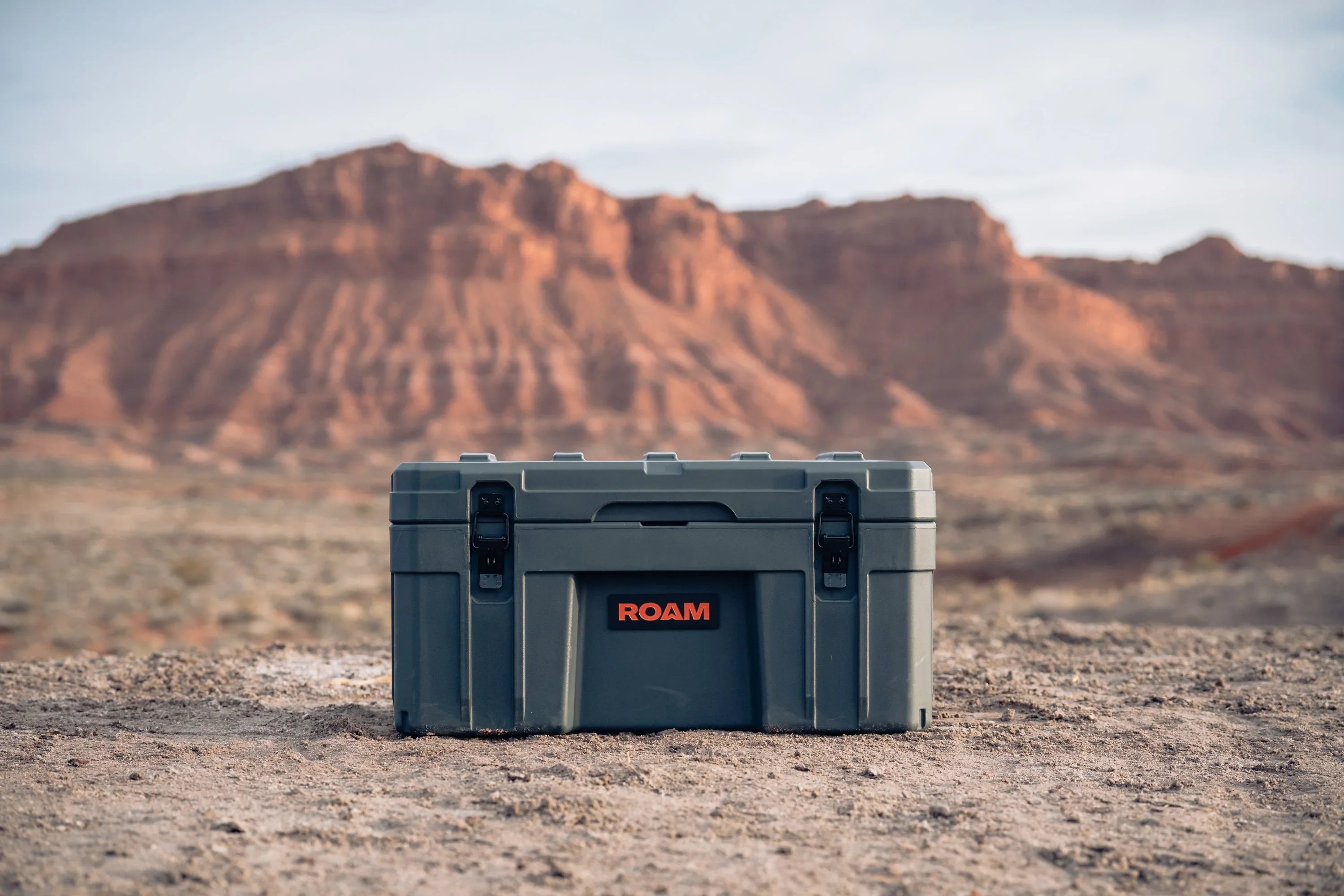 Overland storage box with ROAM logo on desert terrain with red rock mountains in background