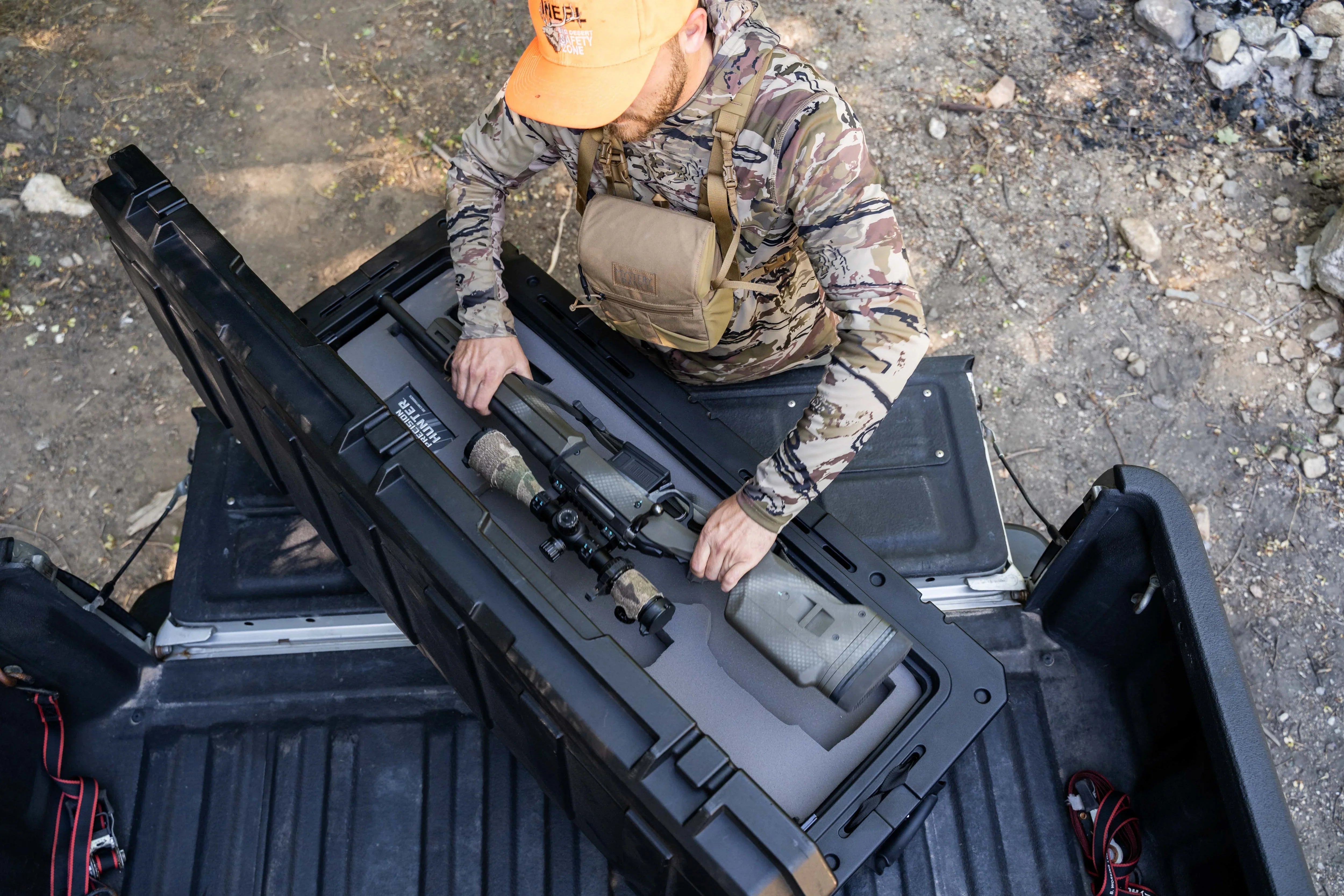 Man in camo gear placing scoped hunting rifle in hard gun case on truck bed outdoors