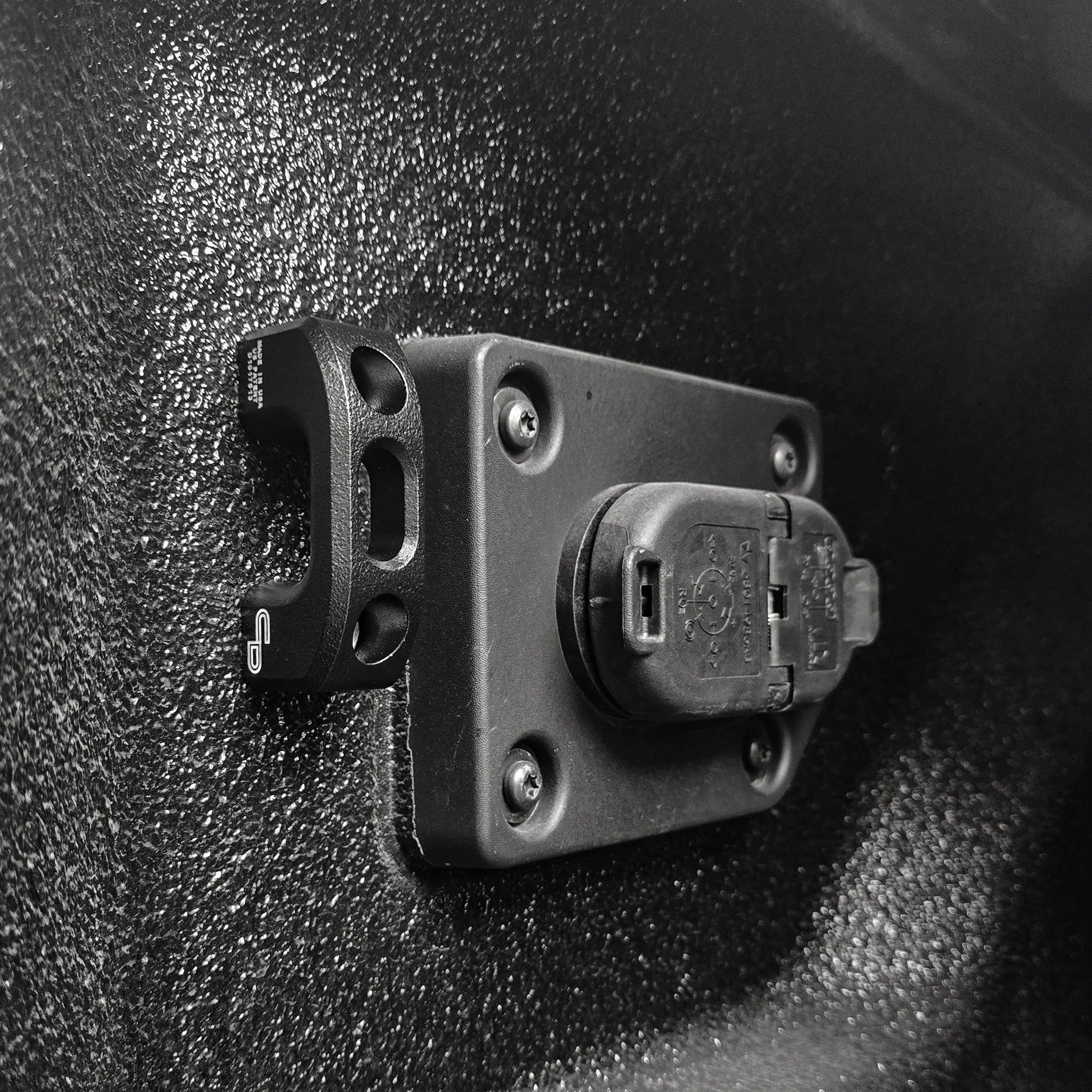 Truck bed tie down anchor and power outlet on textured black surface