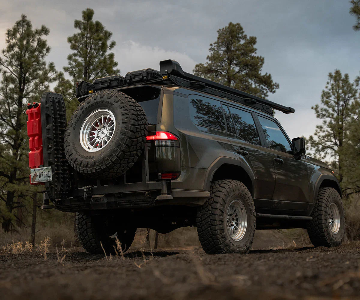 Off-road SUV with expedition gear, roof rack, spare tire, and recovery accessories in forest