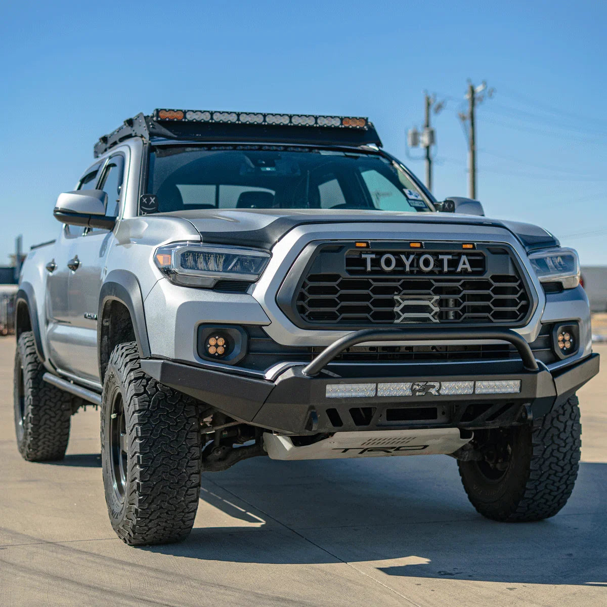 Lifted silver Toyota Tacoma with off-road accessories, roof rack, LED lights, and rugged tires