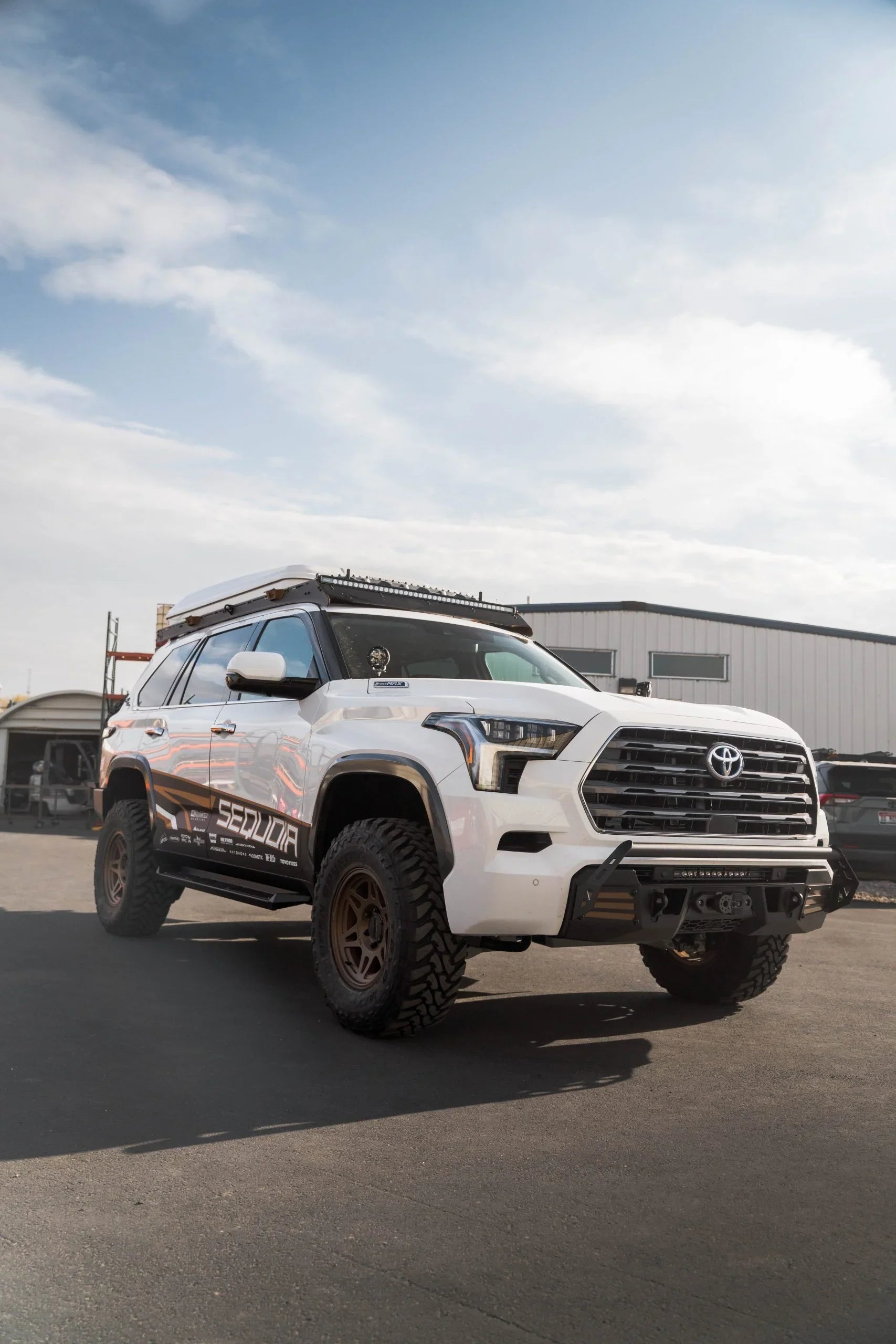 Lifted white Toyota Sequoia SUV with off-road tires and roof rack, parked outdoors