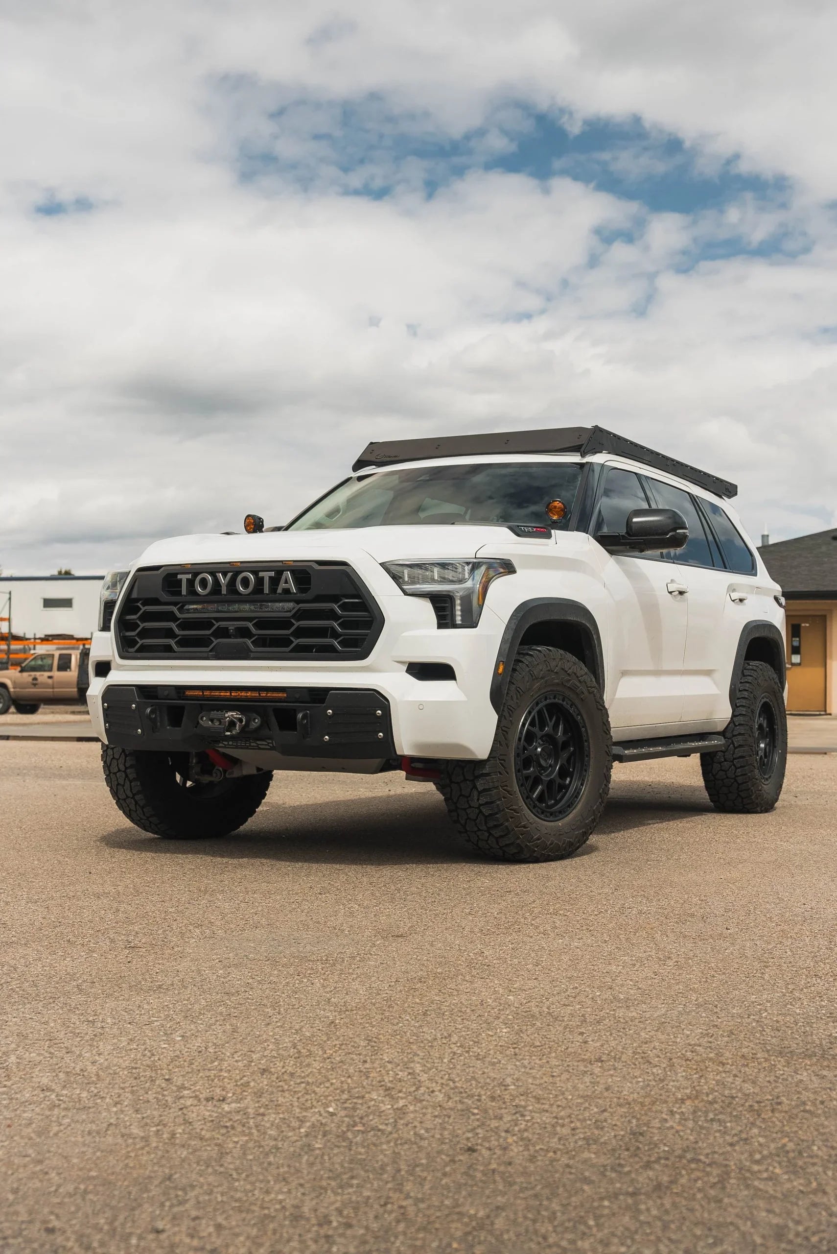 White Toyota SUV with rooftop overland rack and offroad tires parked outdoors