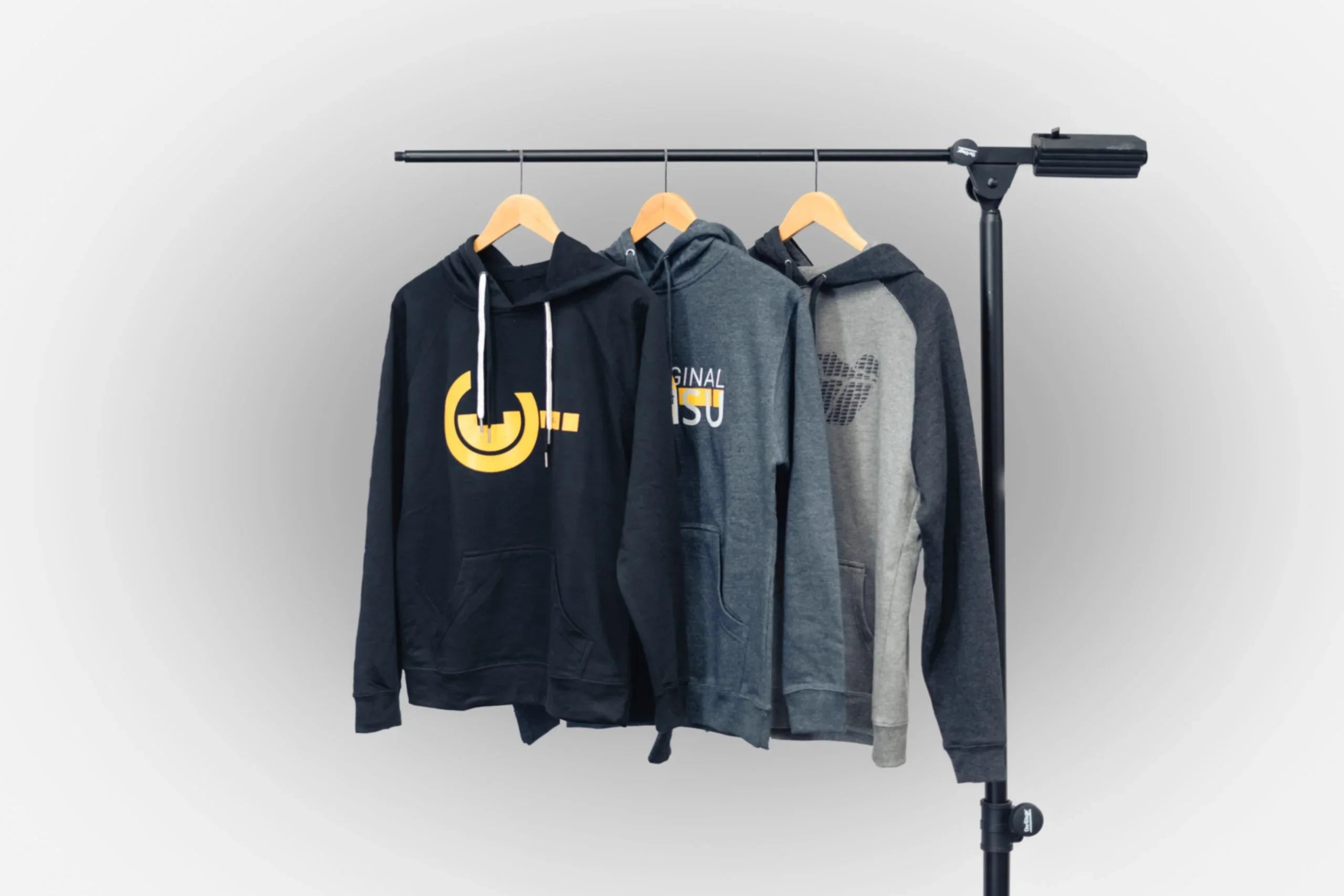 Three hoodies with adventure and outdoor graphics on hangers, displayed on a clothing rack.