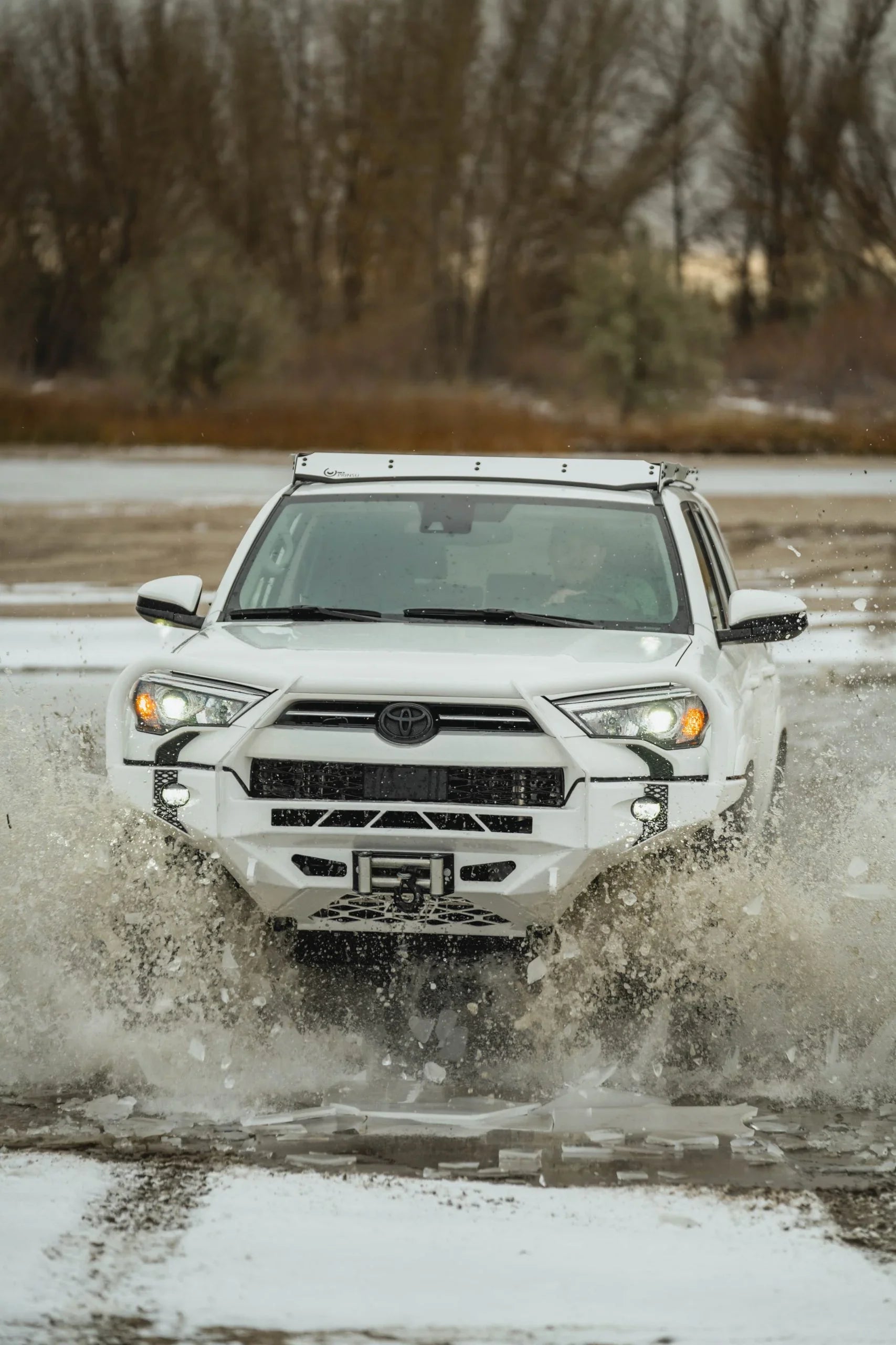 White Toyota 4Runner with off-road accessories driving through icy water outdoors