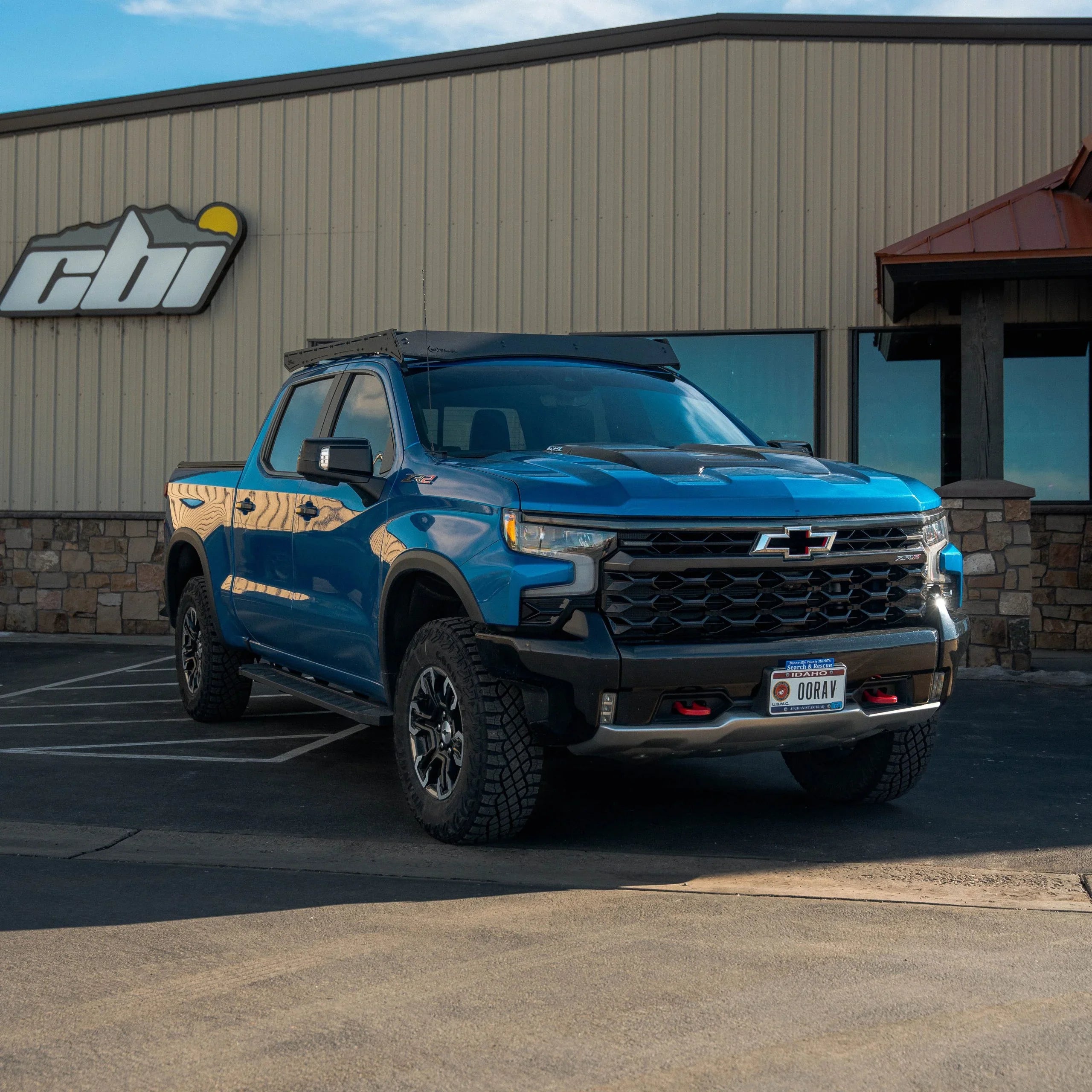 Blue Chevrolet Silverado ZR2 with off-road roof rack parked in front of an outdoor equipment shop
