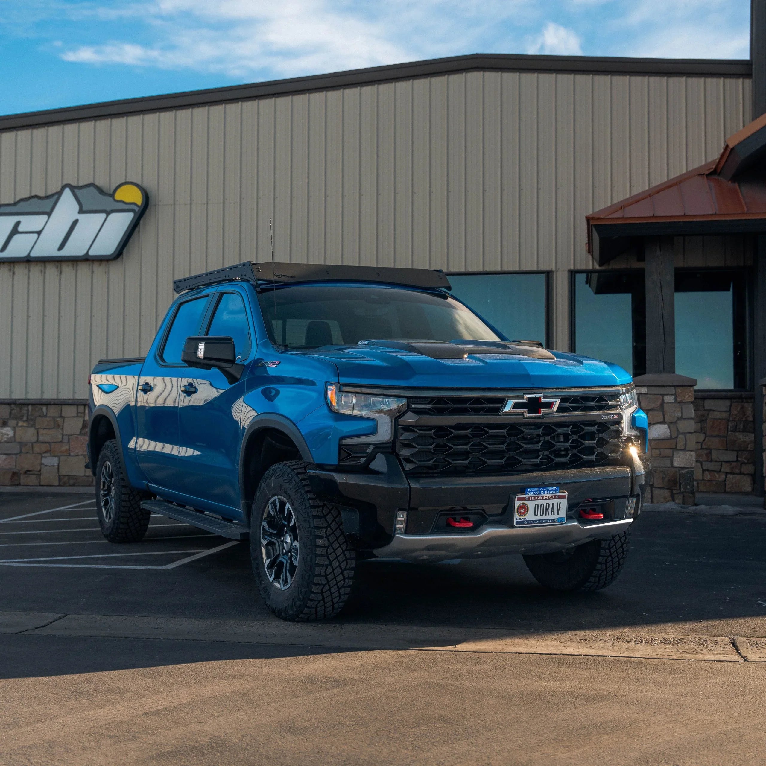 Blue Chevrolet Silverado ZR2 with overlanding roof rack parked outside commercial building
