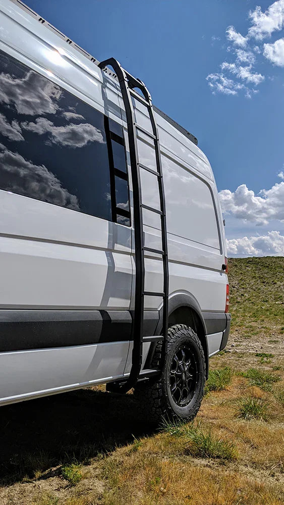 Overlanding Sprinter van with rugged roof rack and side ladder parked on grassy field