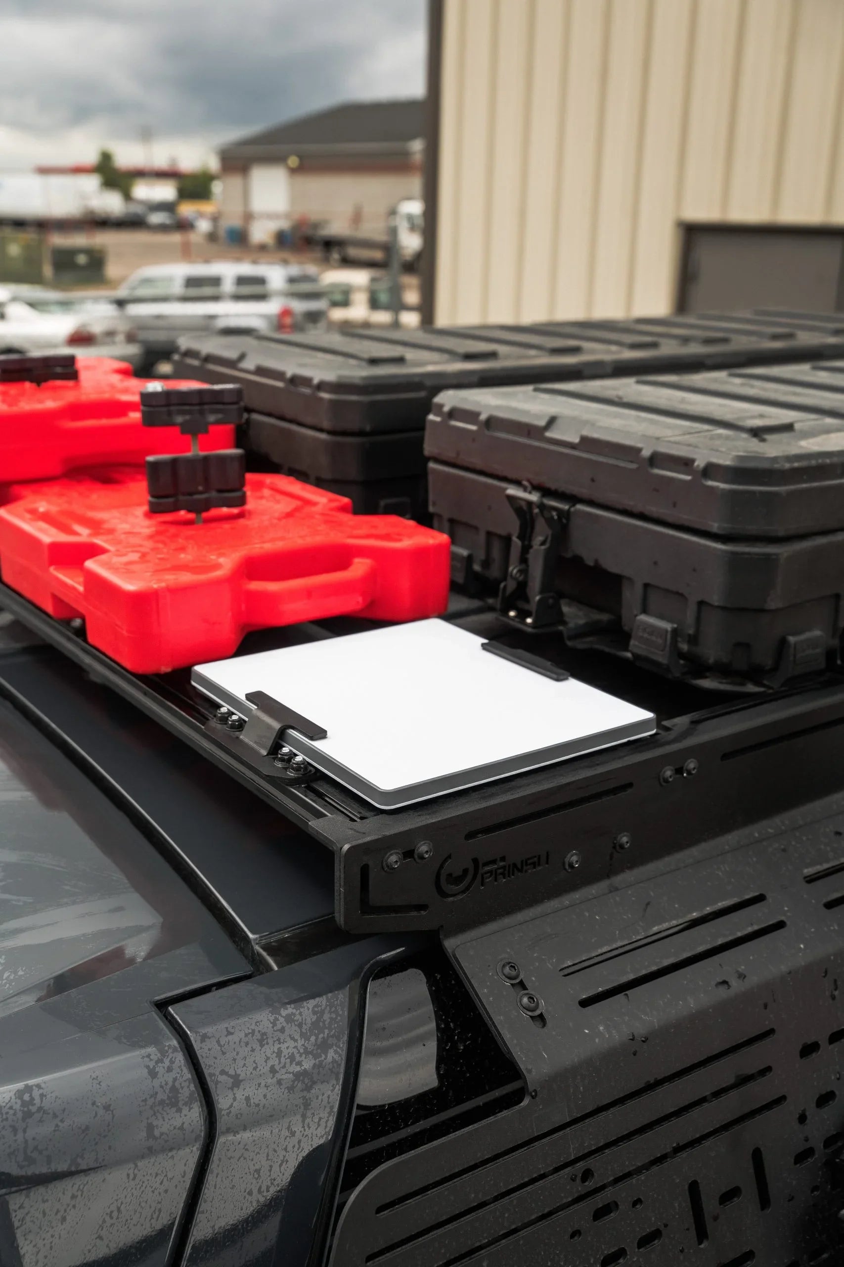Overland vehicle roof rack with black storage cases, red fuel packs, and mounting bracket