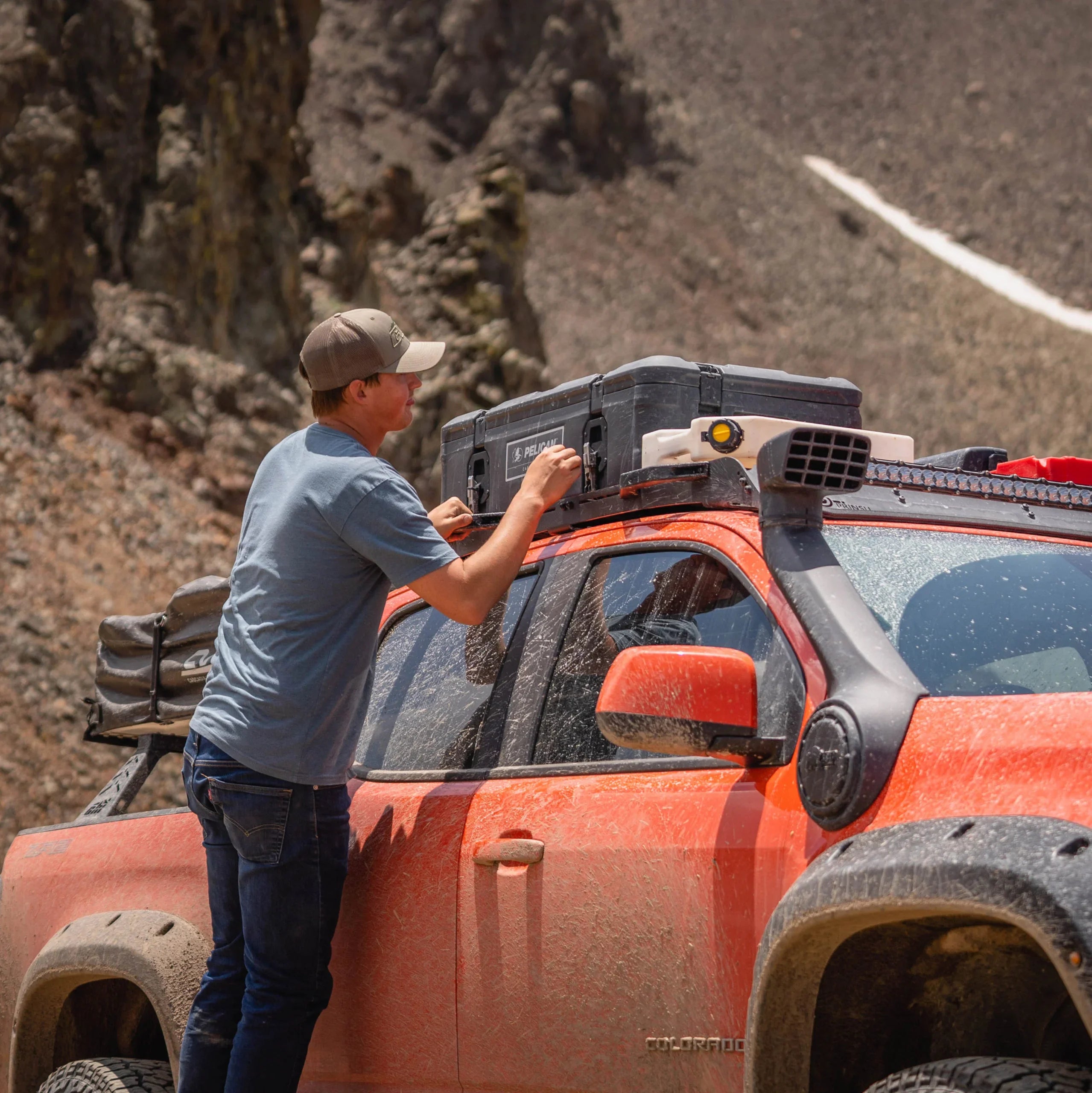 Man securing storage case on Prinsu roof rack of off-road Toyota pickup truck in rugged terrain