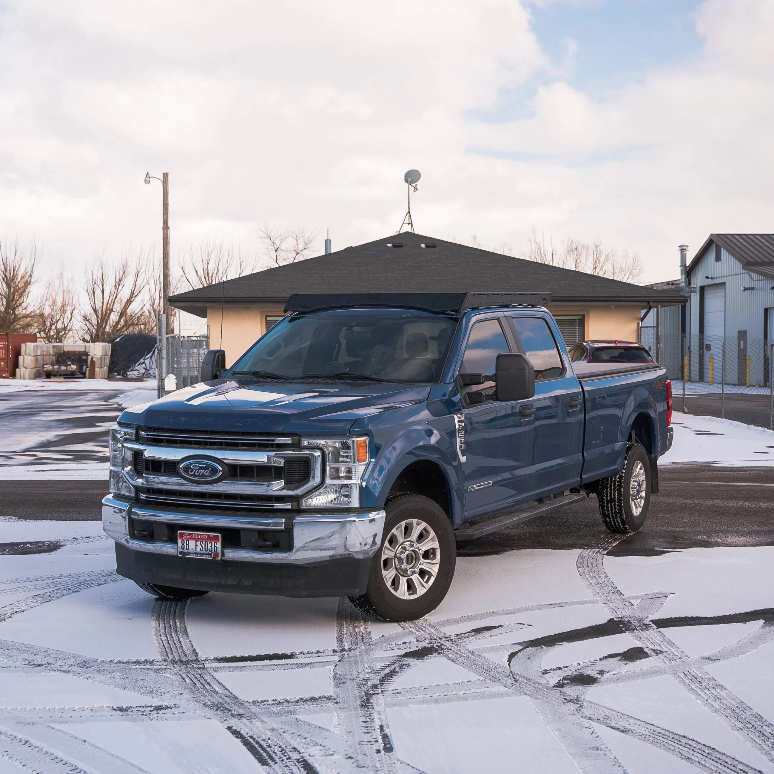 Blue Ford Super Duty pickup truck parked on snowy pavement near garage buildings