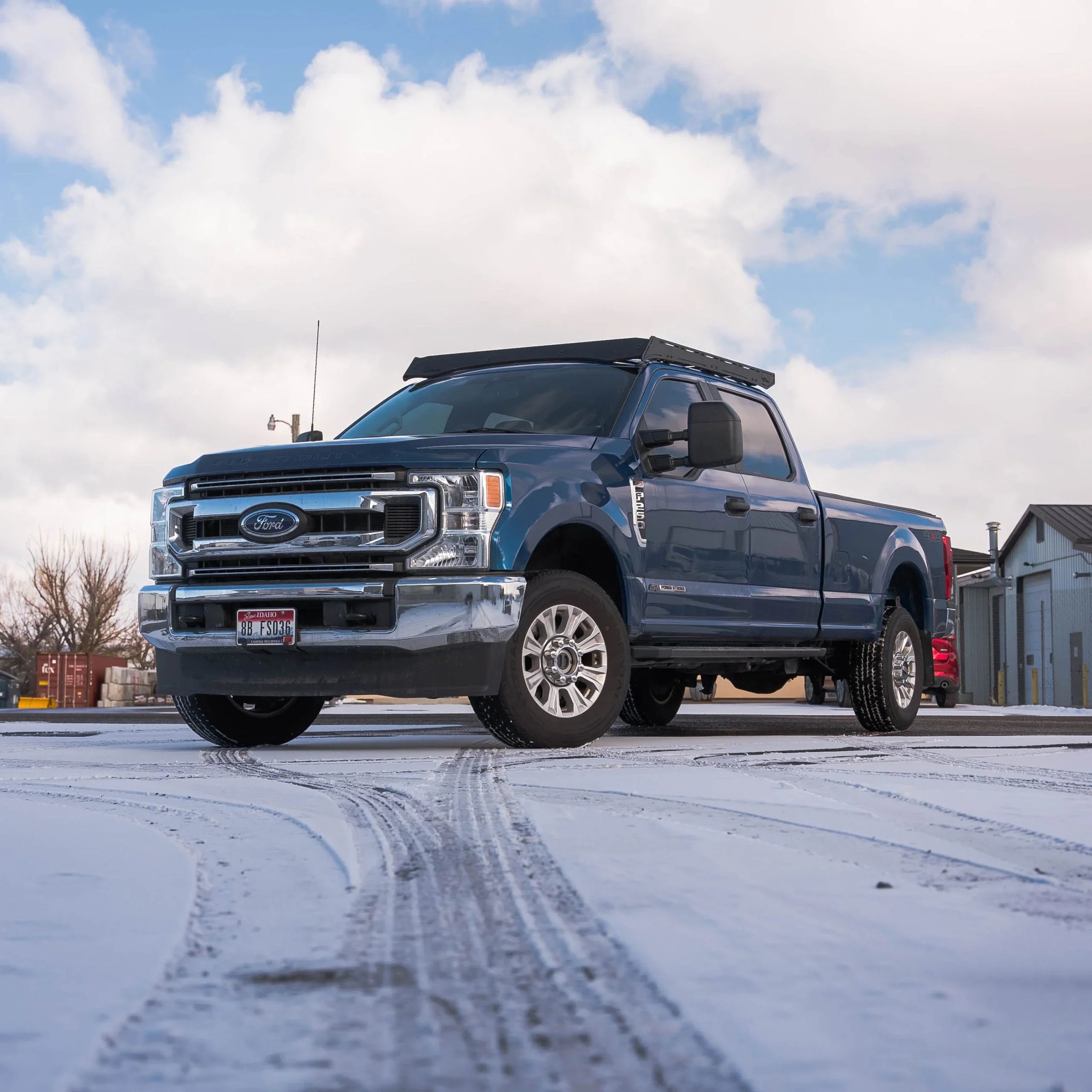 Blue Ford Super Duty pickup truck outfitted with roof rack for overlanding in snowy parking lot