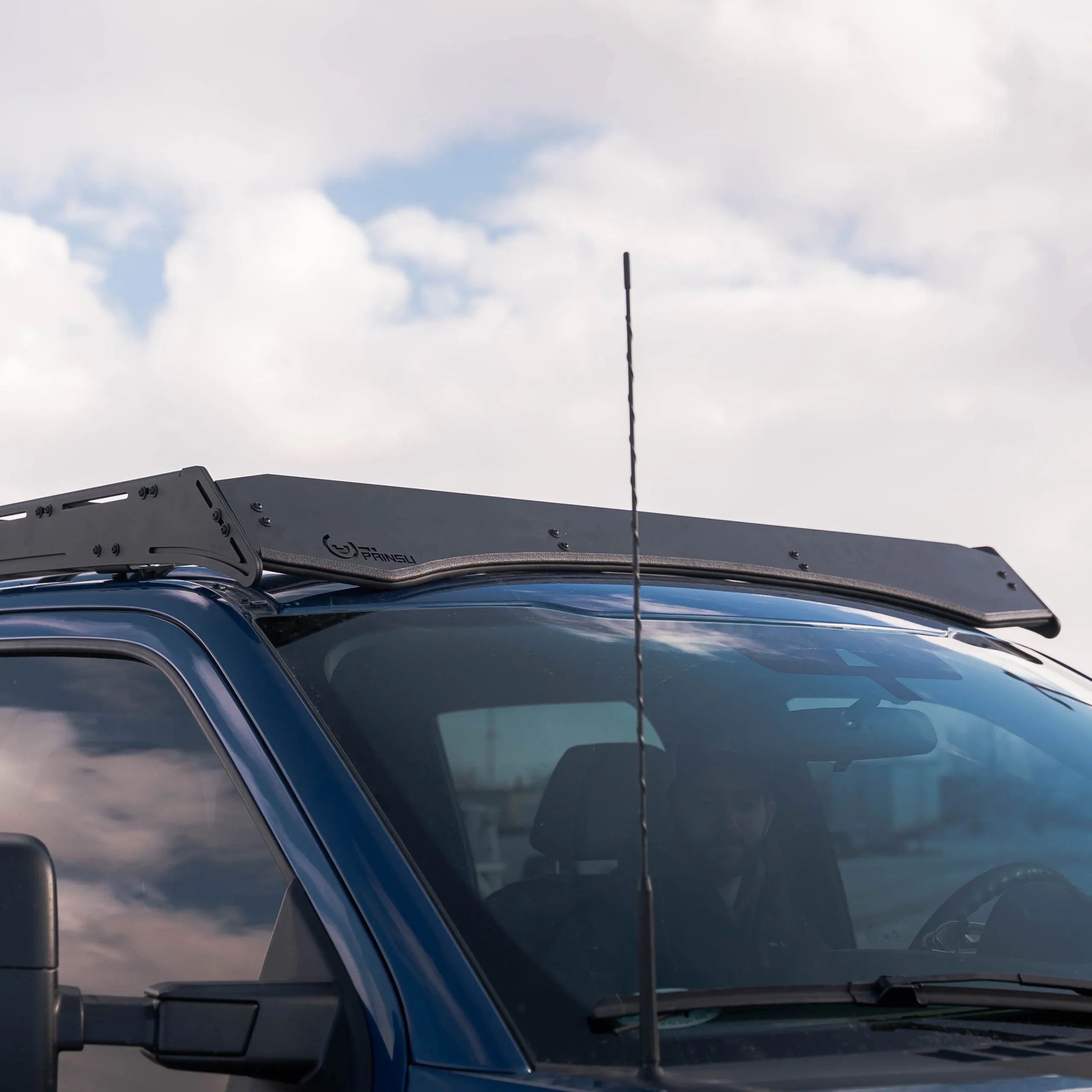 Black roof rack mounted on blue truck cab, outdoors under cloudy sky, overlanding gear