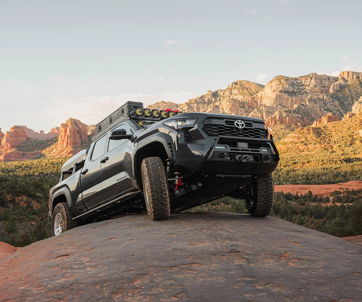 Toyota Tacoma overlanding truck with rooftop tent and KC lights on rocky desert trail