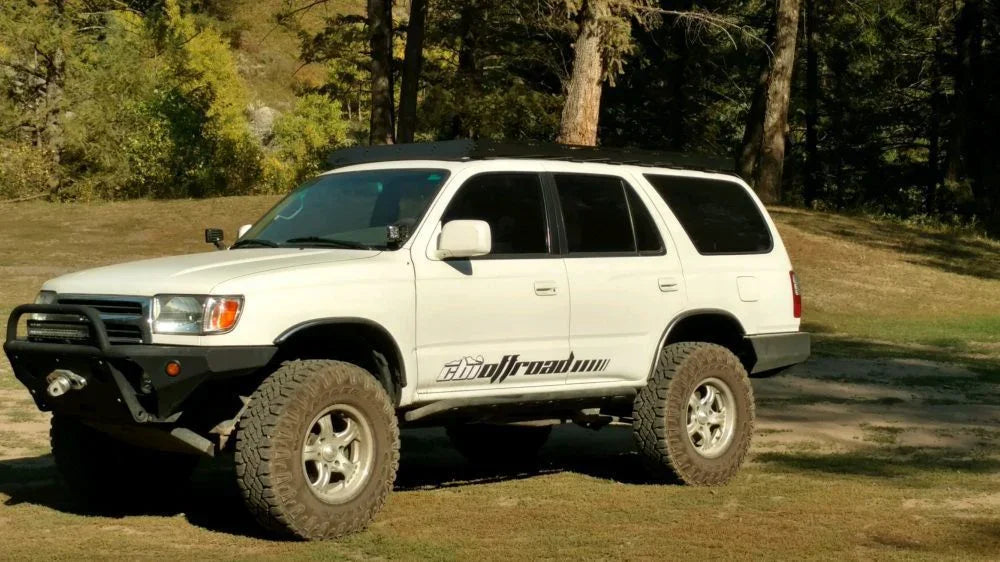 White Toyota 4Runner with off-road tires and roof rack in a forested outdoor setting