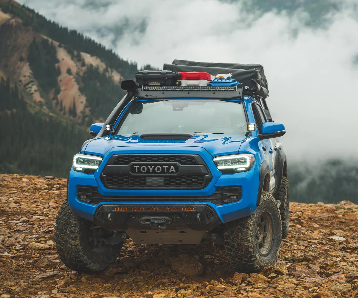 Blue Toyota Tacoma 3rd gen with Covert front bumper, off-road gear, on rocky mountain trail