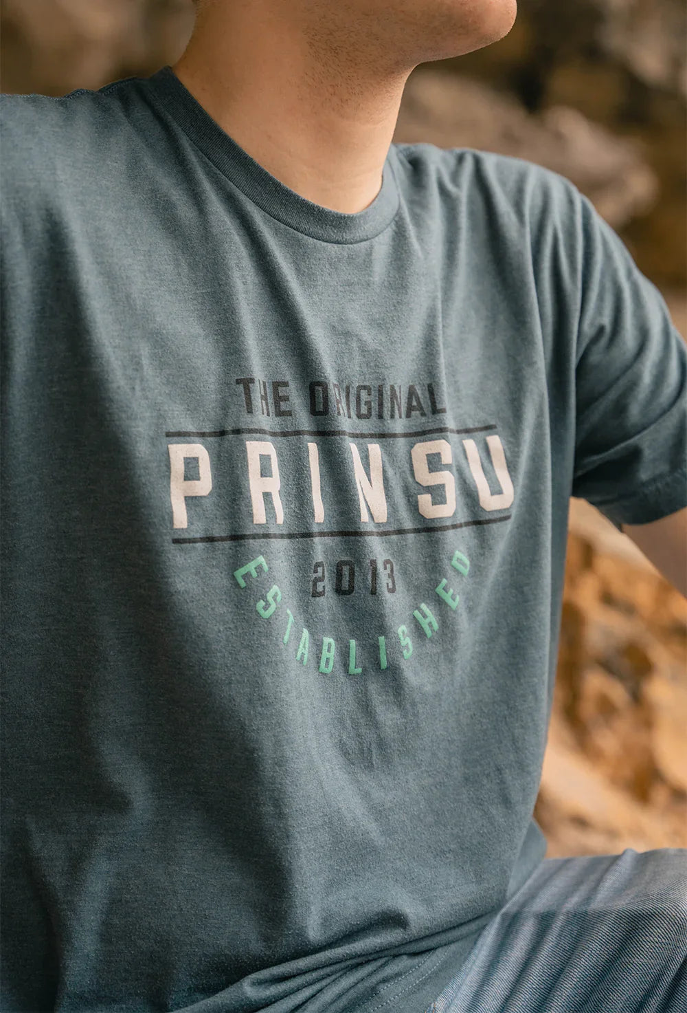 Person wearing blue Prinsu t-shirt with 'The Original Prinsu Established 2013' graphic outdoors