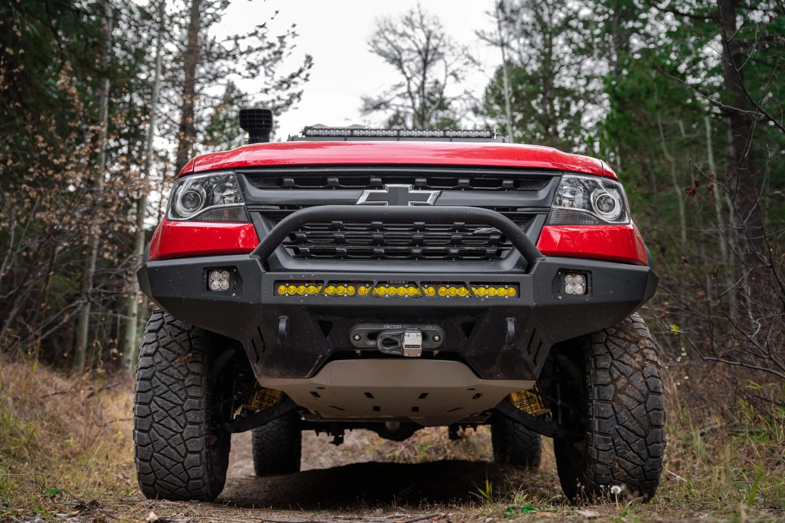 Red Chevrolet Colorado off-road truck with rugged bumper and LED light bar on forest trail