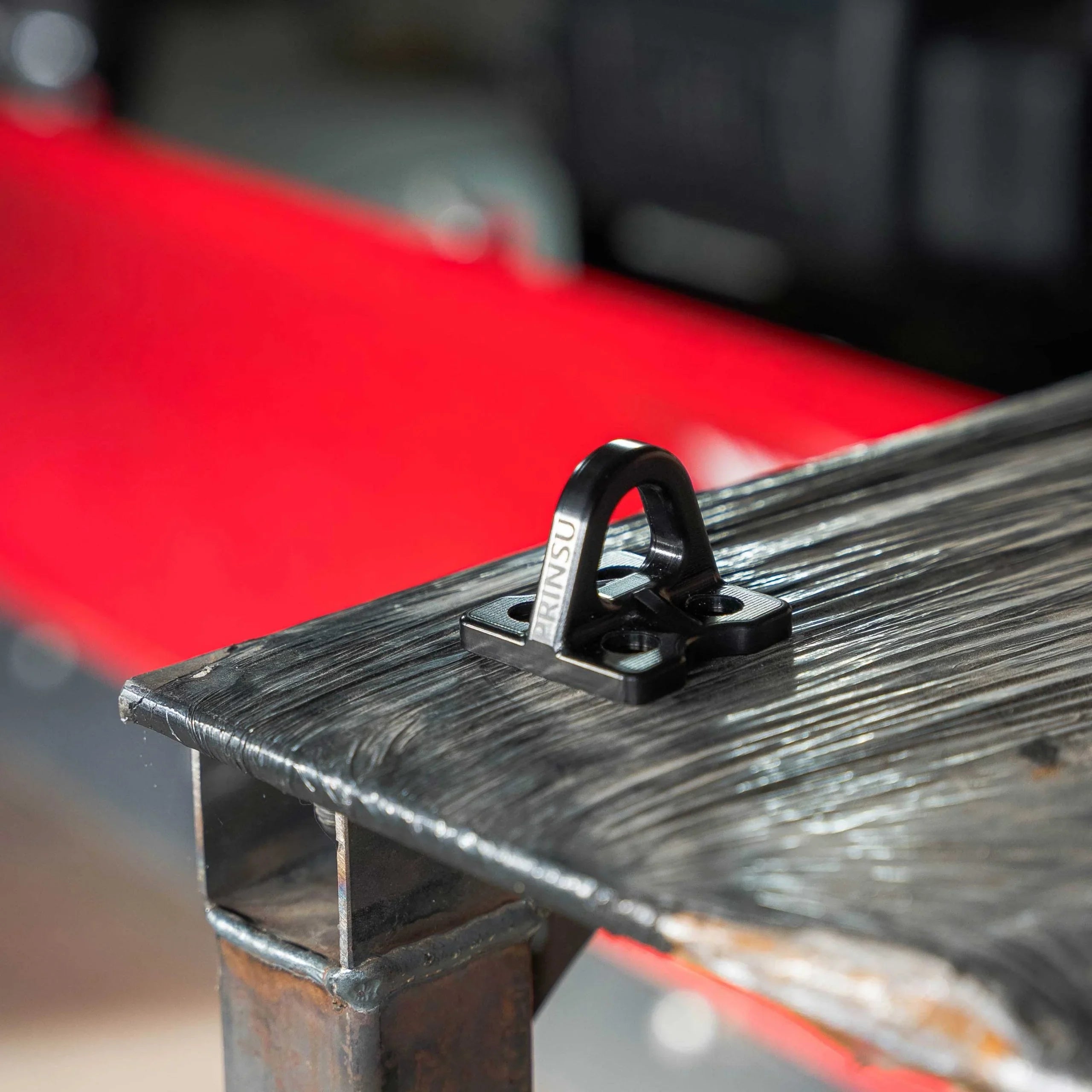 Black metal tie down point mounted on a rugged truck bed rail for overlanding gear securing.