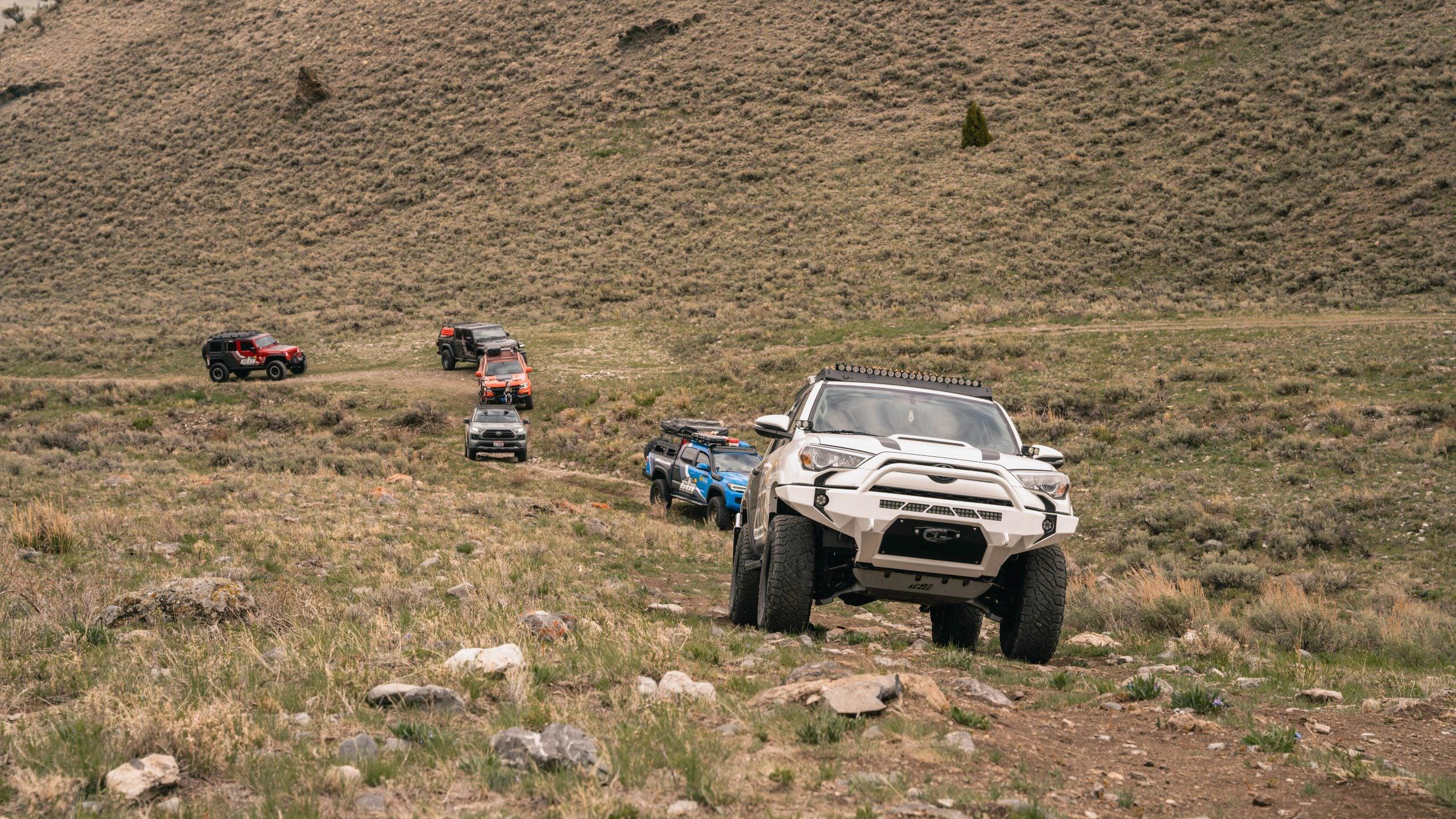 Toyota 4Runner, Tacoma, Jeep SUVs and trucks off-roading on a rocky grassy trail