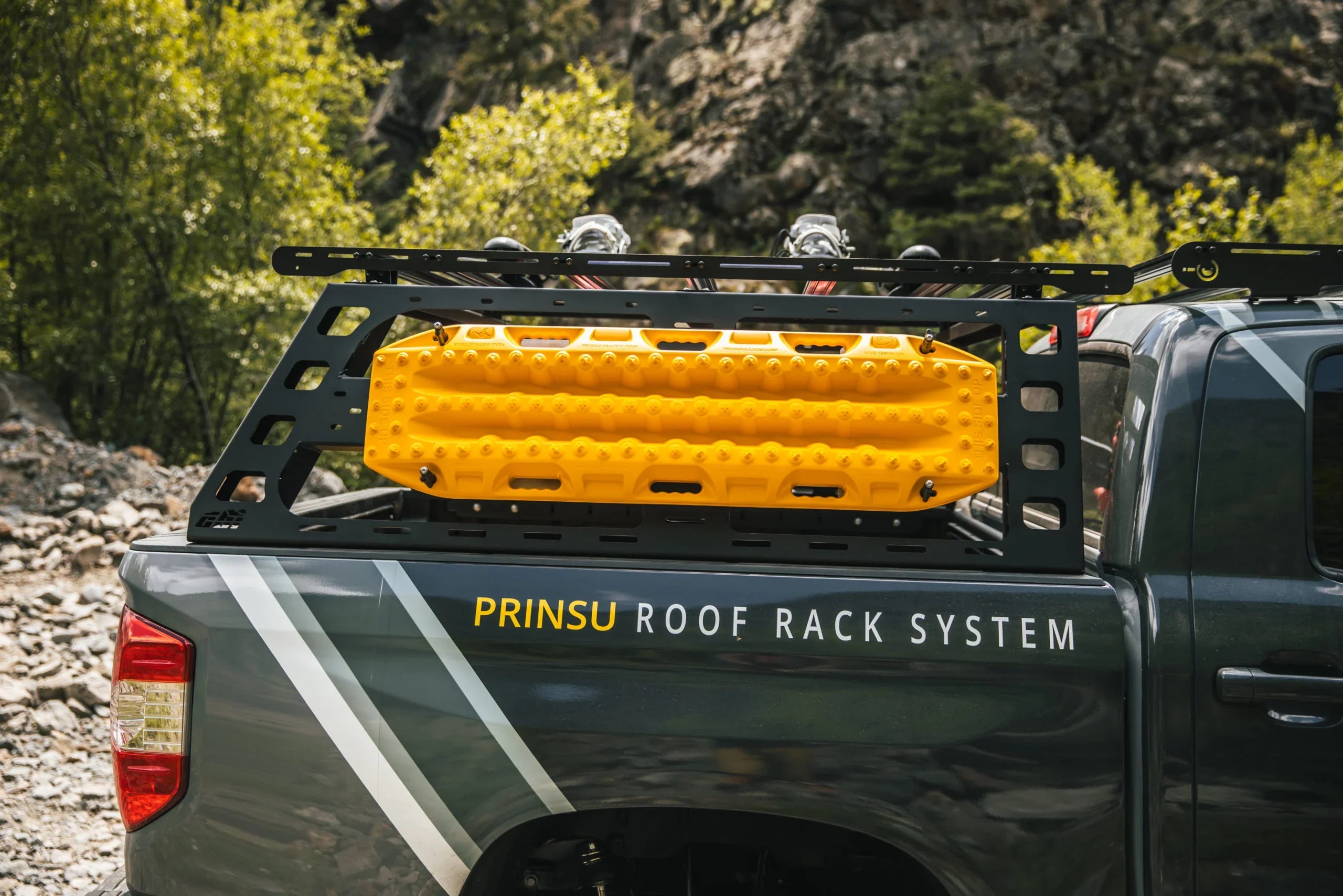 Toyota Tundra bed rack with yellow recovery boards mounted, parked outdoors on rocky terrain
