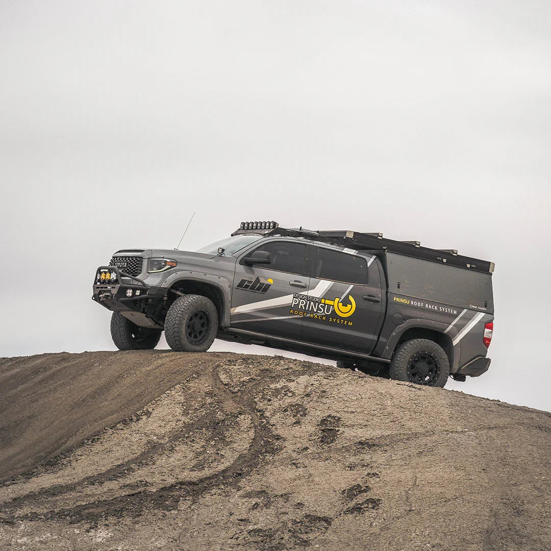 Toyota Tundra with overland rock sliders on a dirt hill, equipped for adventure camping