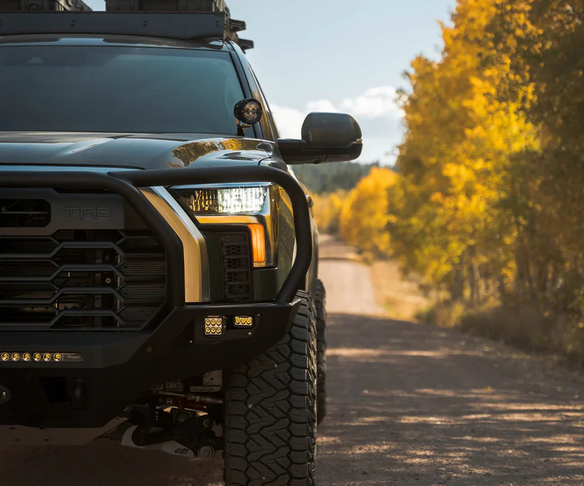 Toyota Tundra with off-road front bumper, LED lights, on a forest dirt road in autumn