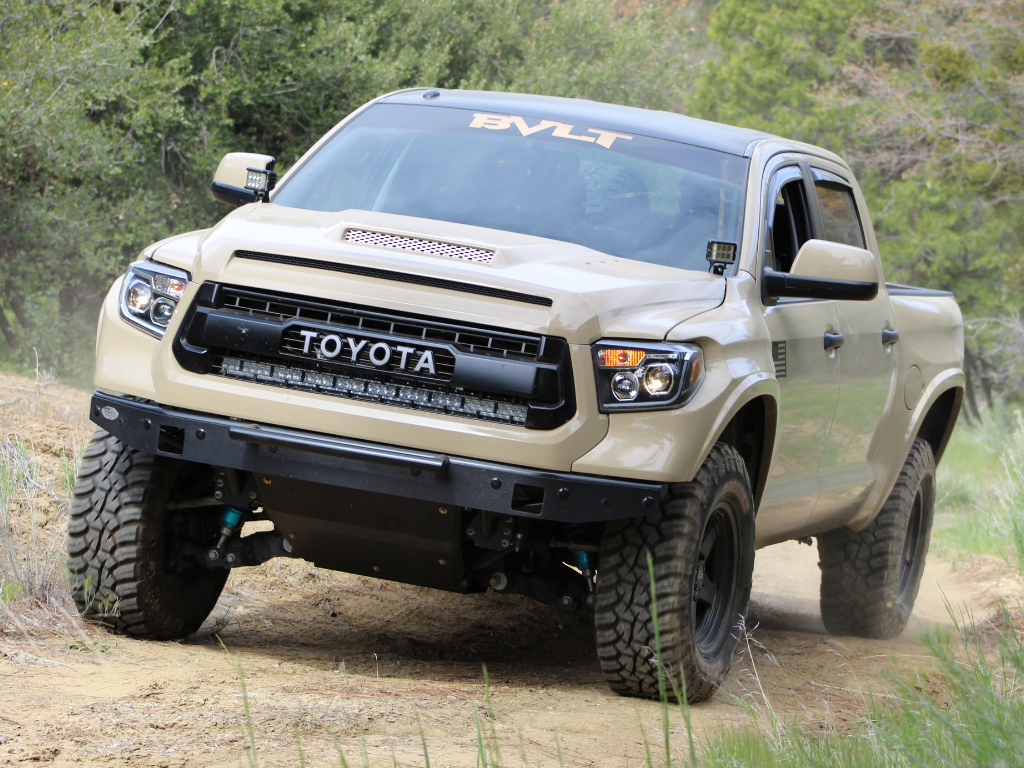 Toyota Tundra with grille light bar off-roading on dirt trail, rugged all-terrain tires