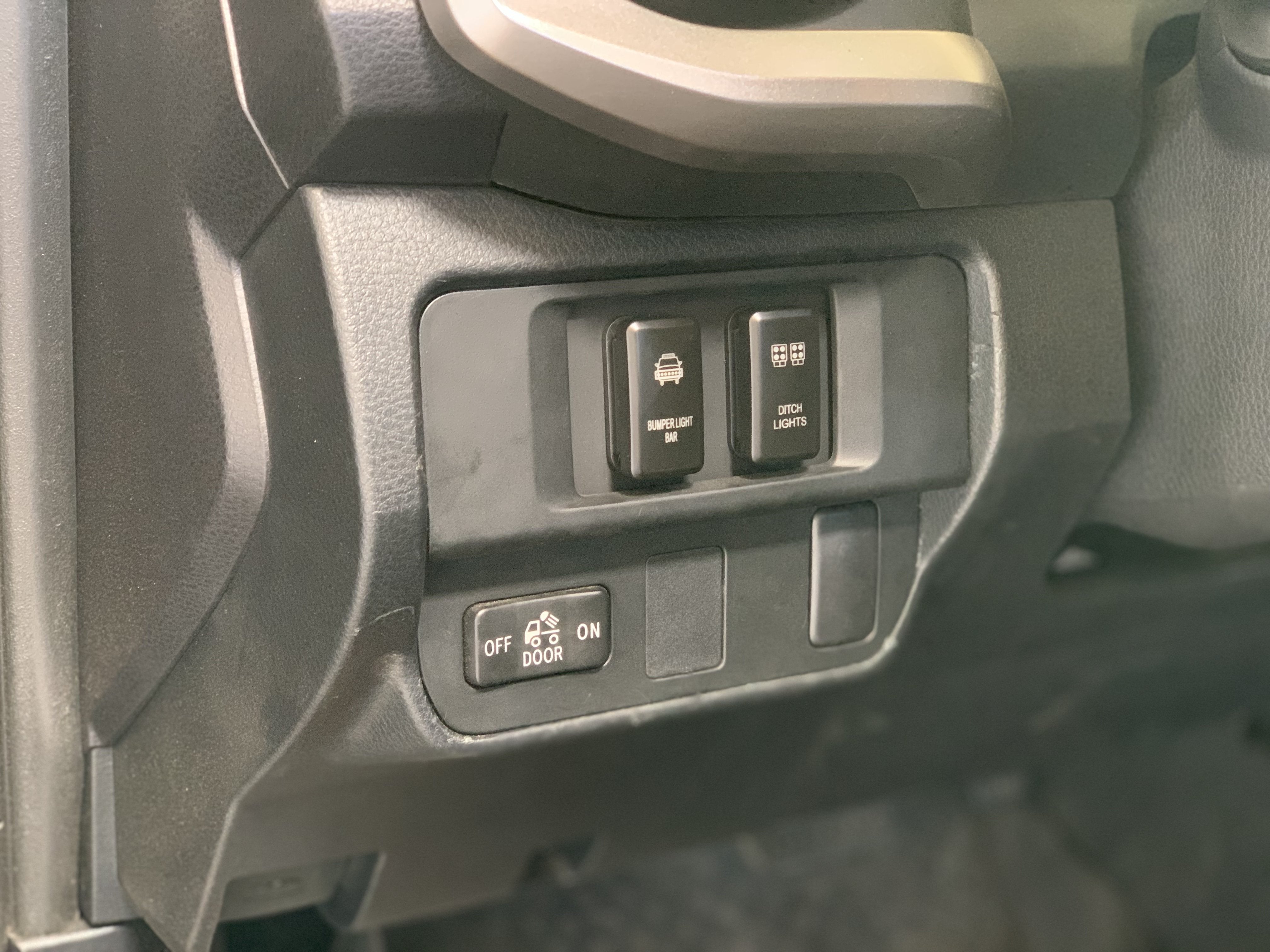 Close-up of vehicle dashboard switches for bumper light bar and ditch lights, off-road accessory controls.