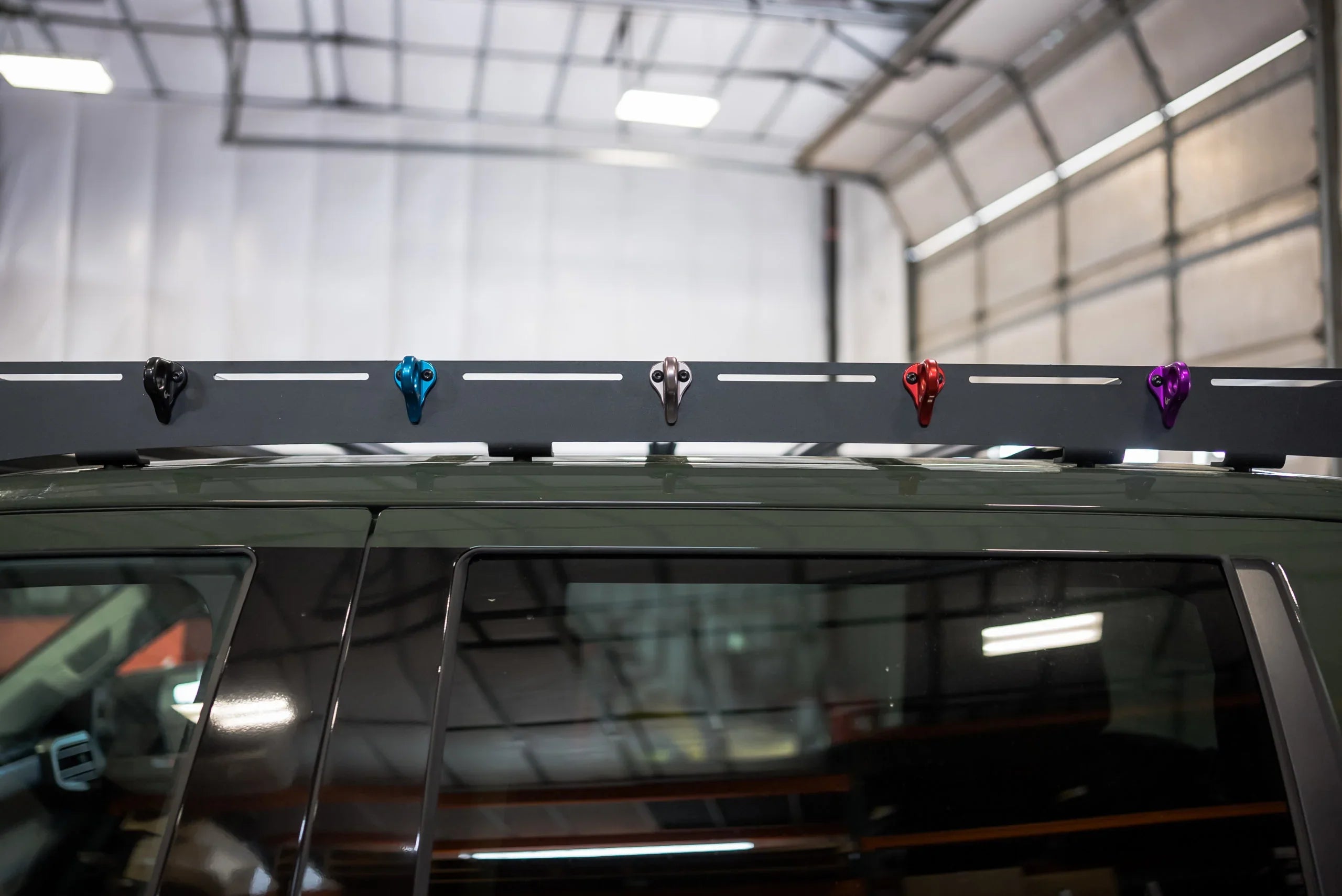 Multi-color utility hook mounts installed on a vehicle roof rack in a garage setting