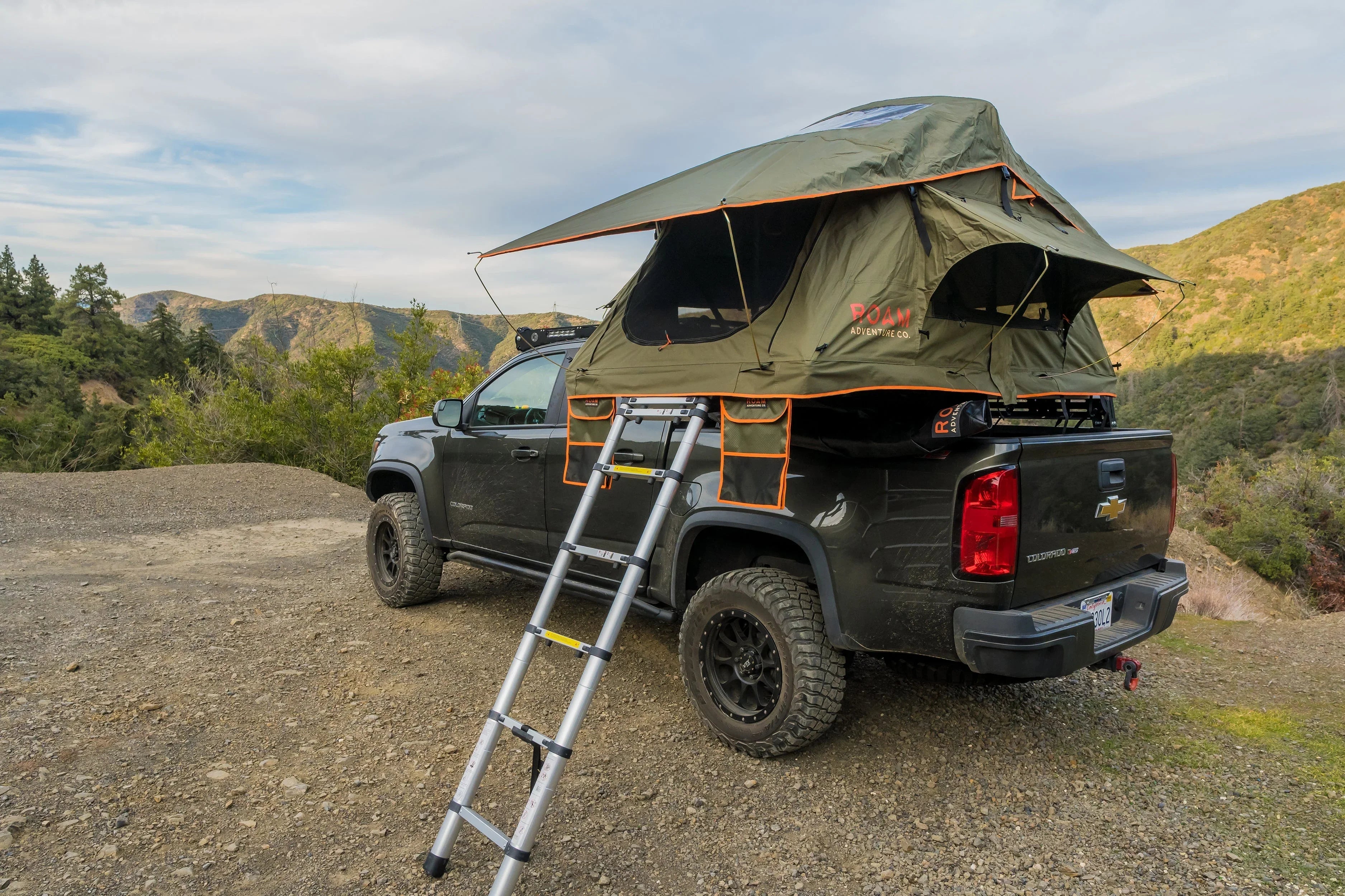 Chevrolet Colorado truck with roof top tent and ladder set up for overland camping in mountains