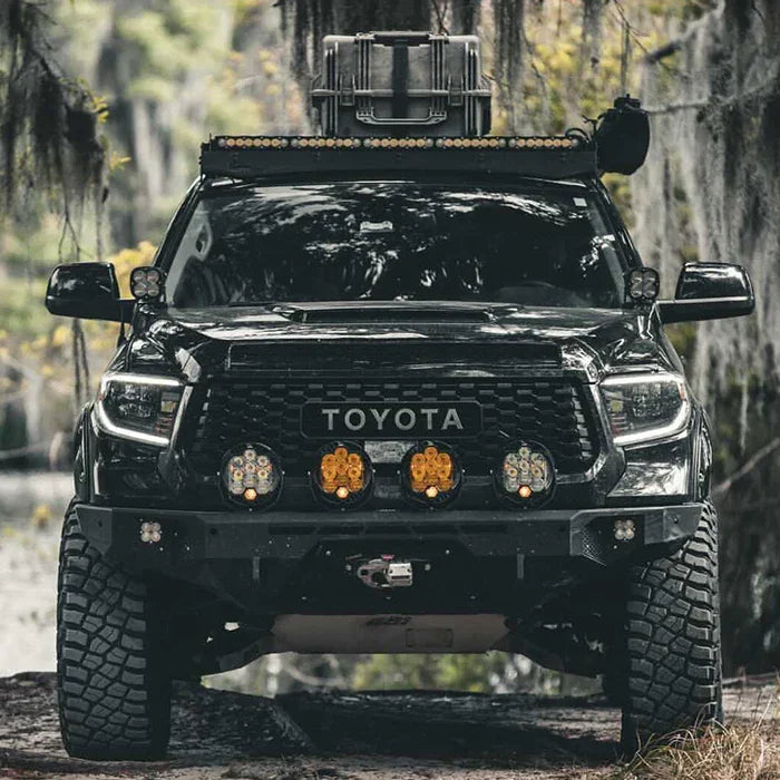 Front view of lifted Toyota truck with off-road bumper and auxiliary lights in a forest