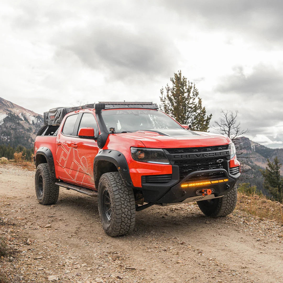 Off-road Chevy Colorado with rock sliders on a mountain trail, overlanding gear visible