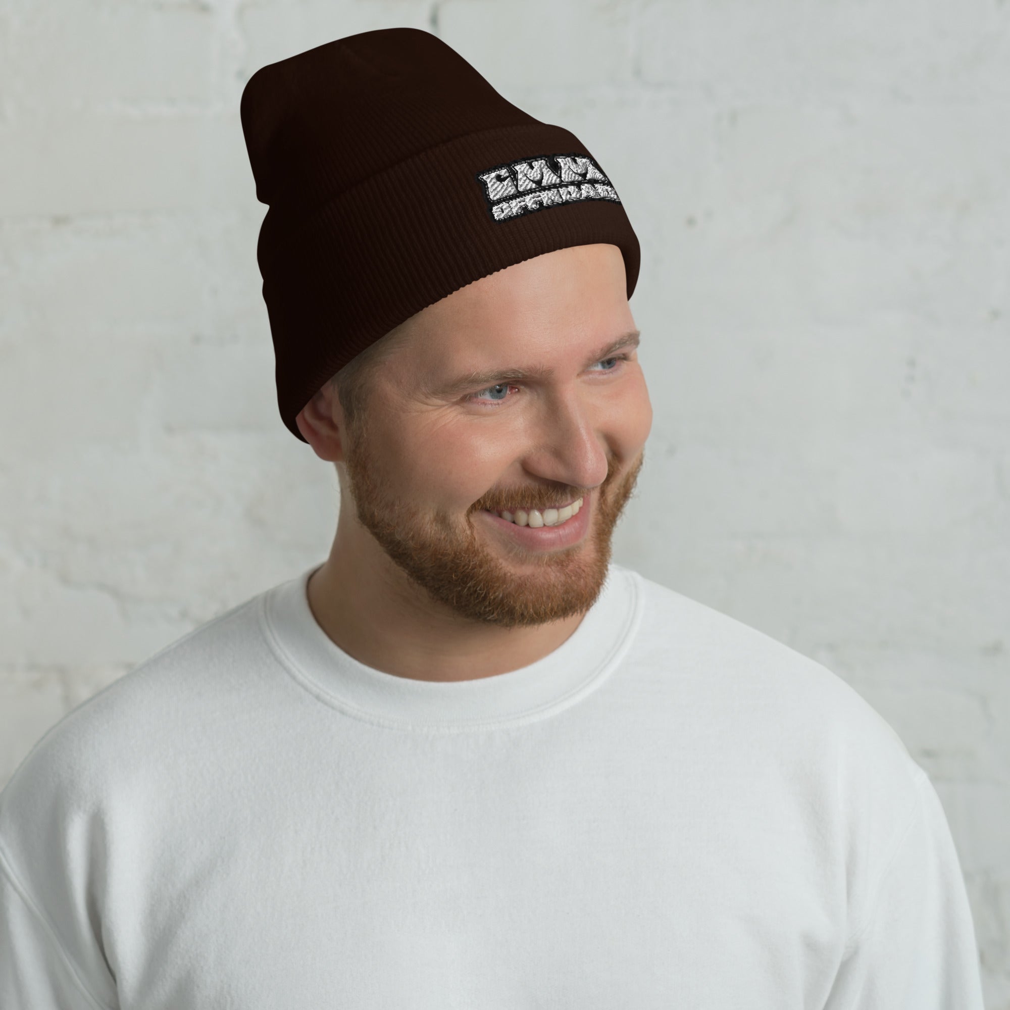 Man wearing a brown cuffed beanie with white text logo, casual outdoor style