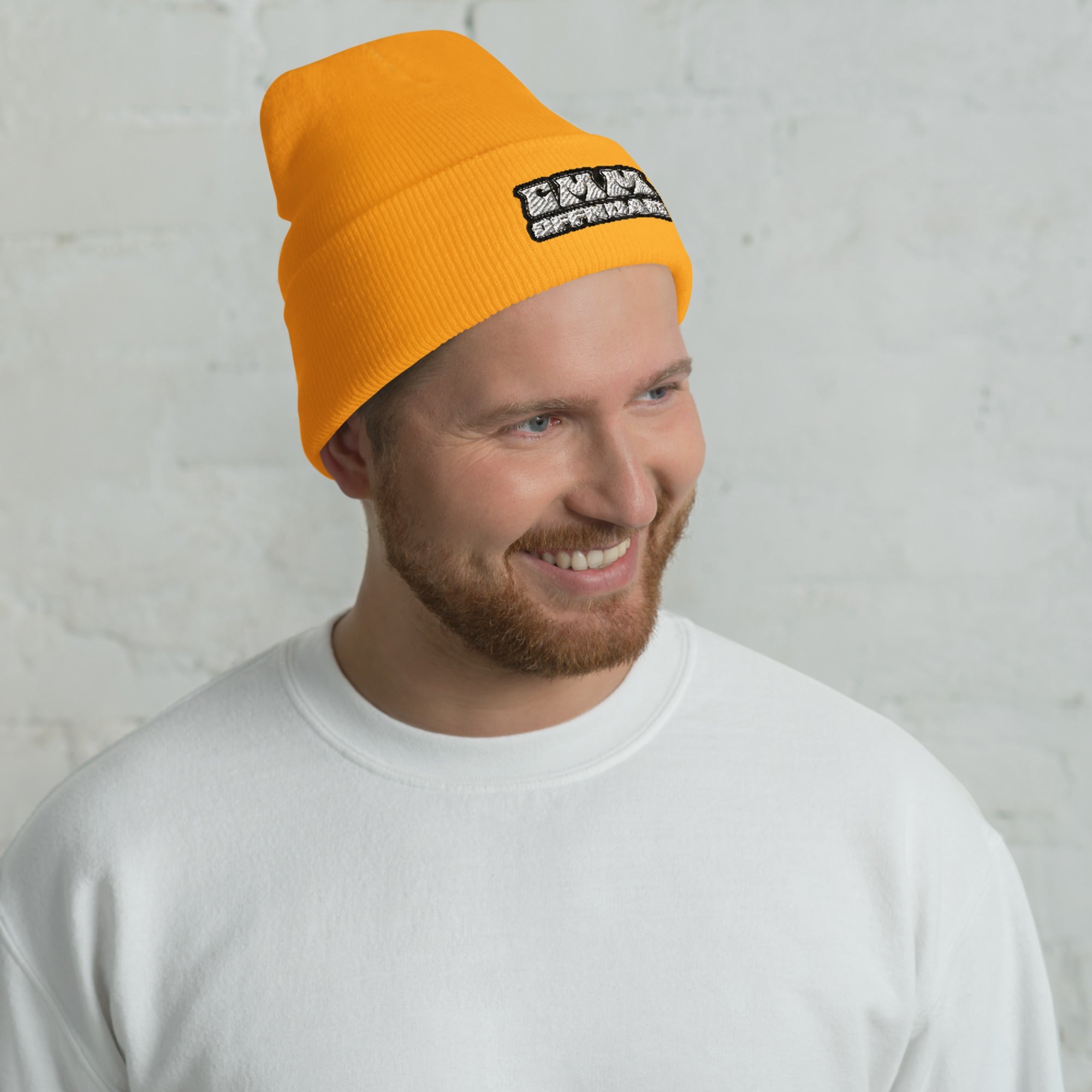 Man wearing gold cuffed beanie with patch, casual white crewneck, indoor setting