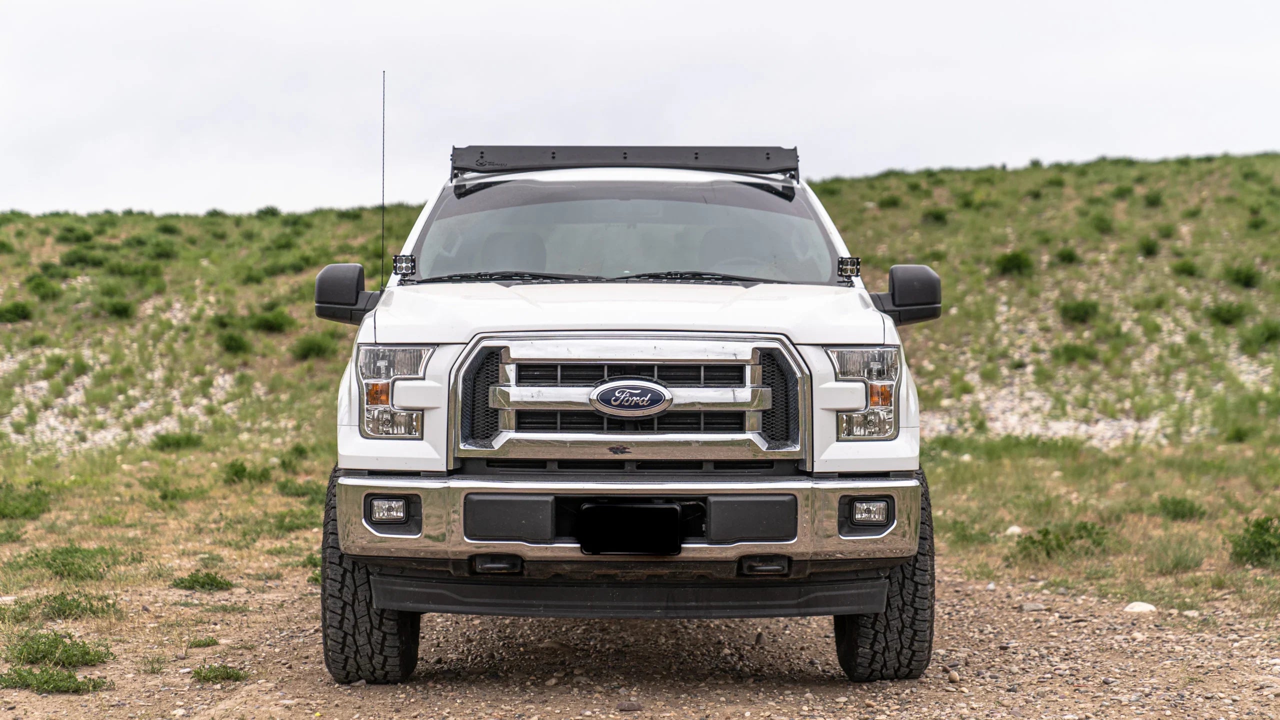White Ford F-150 with off-road roof rack parked outdoors on dirt road