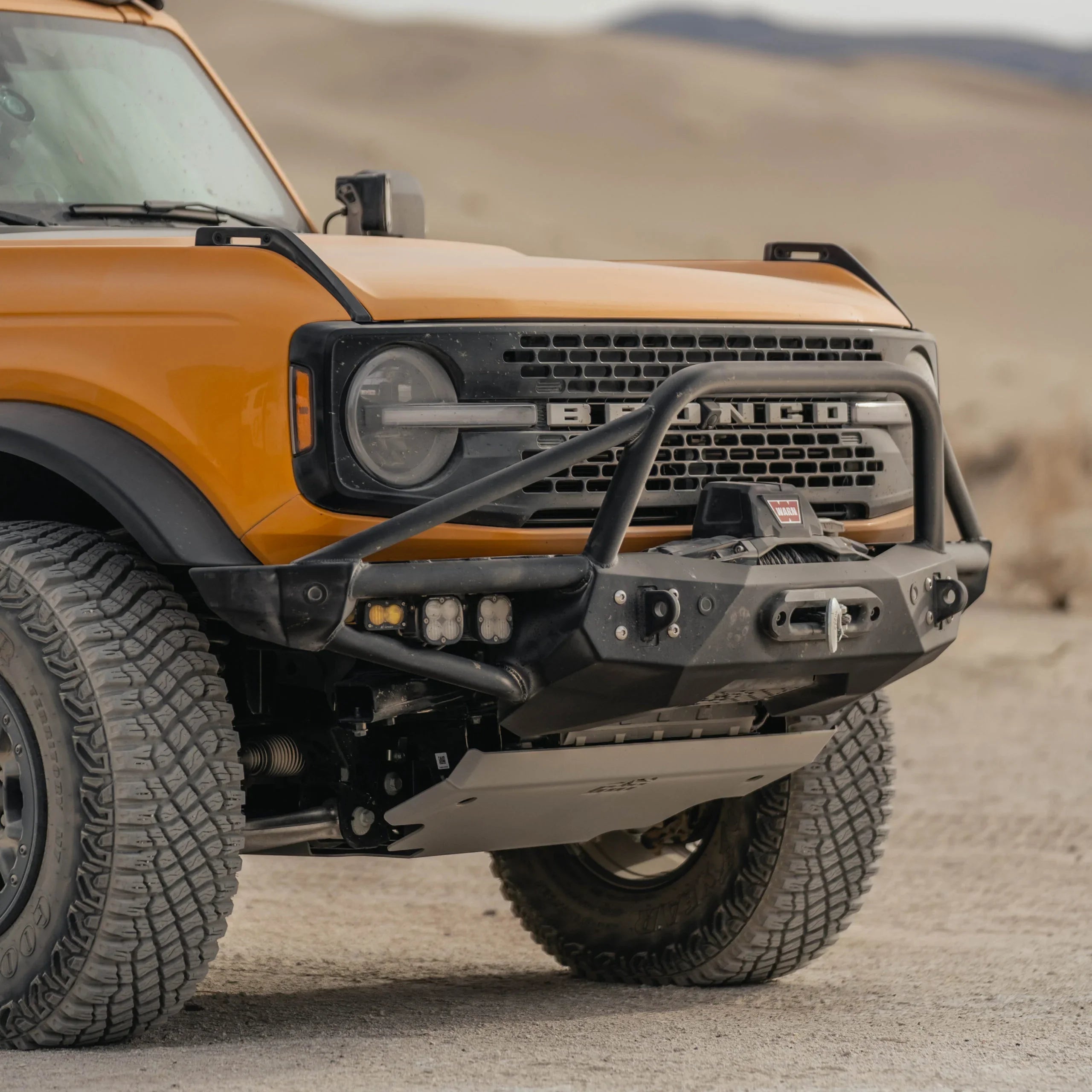 Orange Ford Bronco with off-road front bumper, winch, and rugged tires on desert terrain