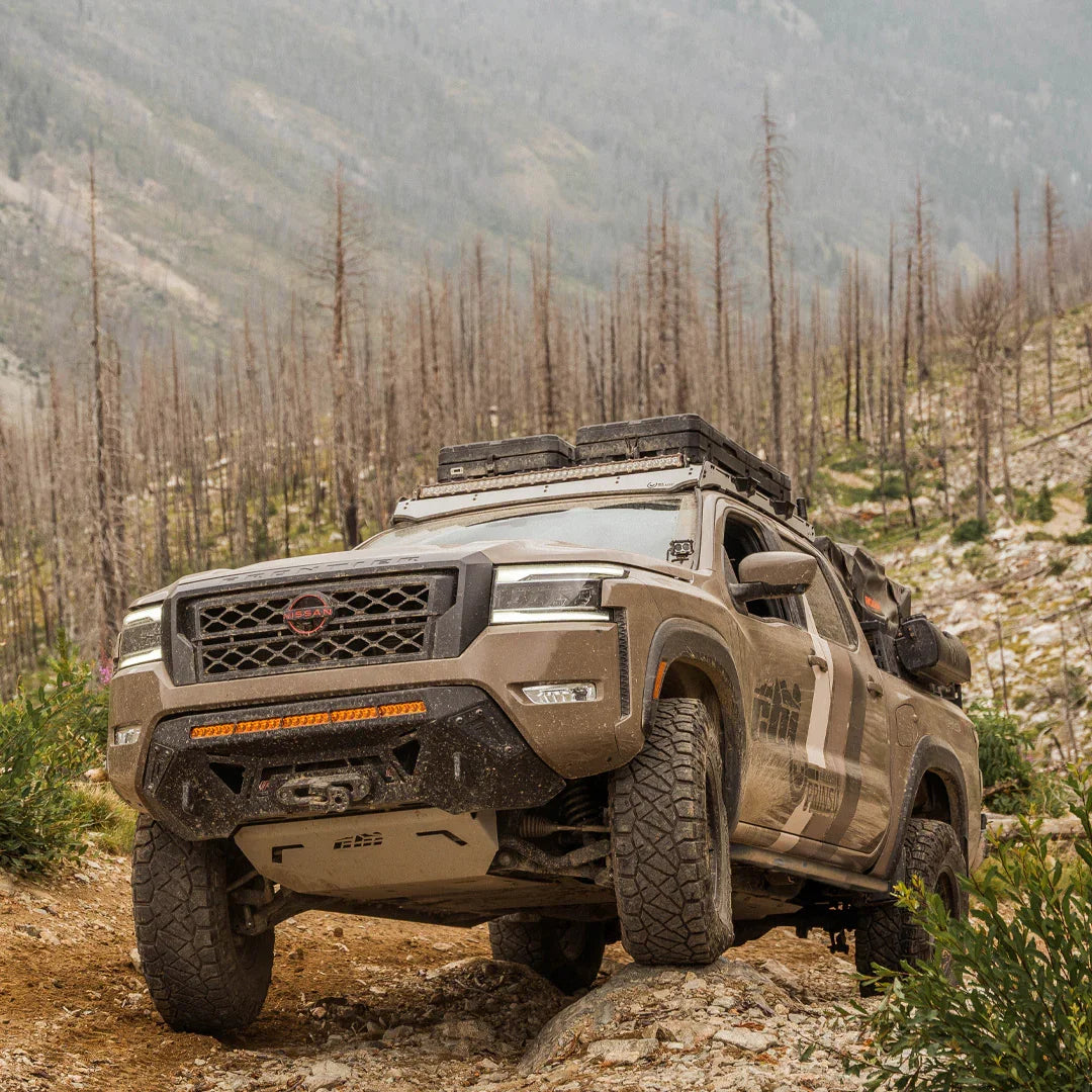 Off-road Nissan Frontier with rock sliders navigating rocky trail, overland gear mounted