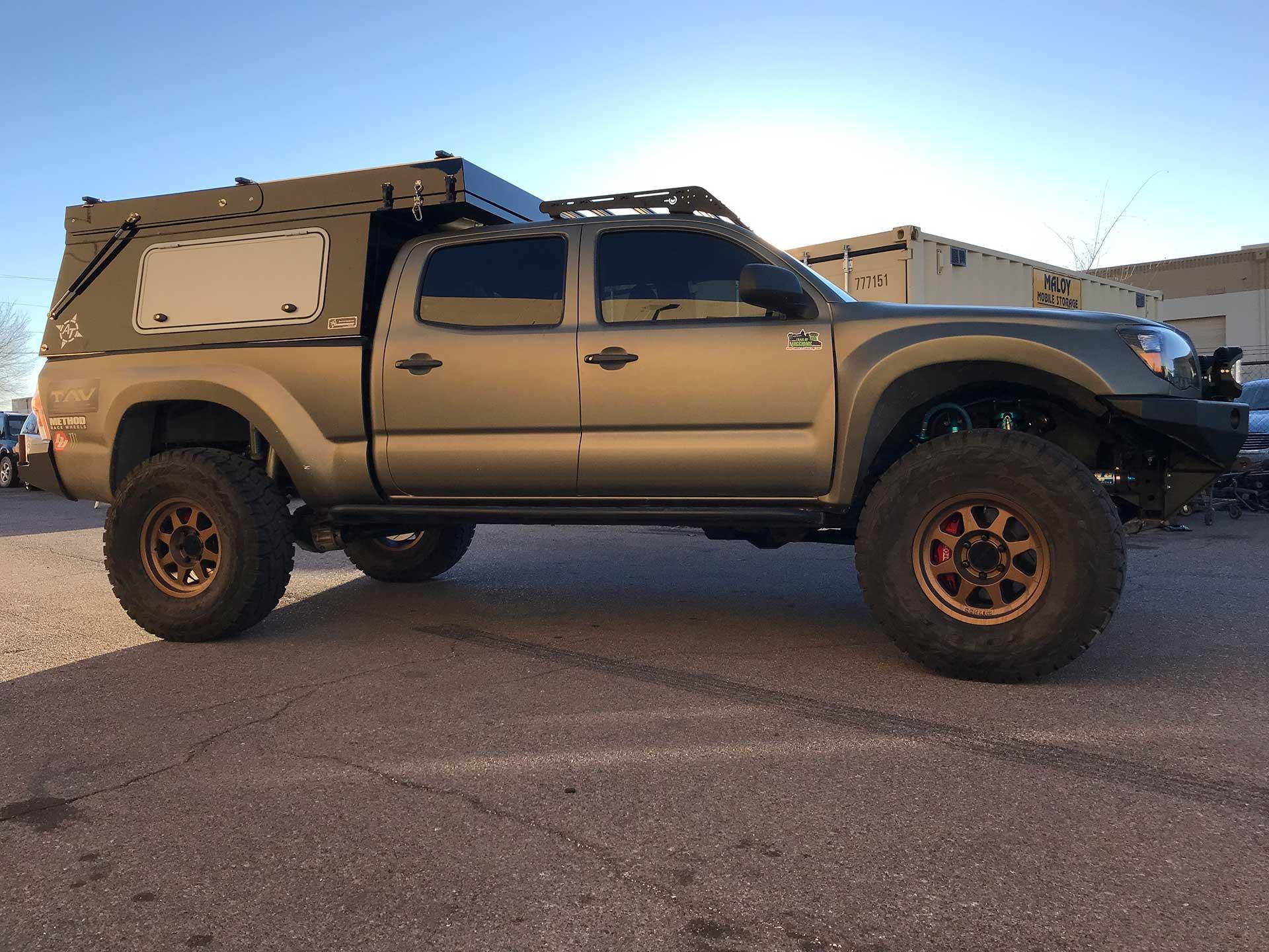 Toyota Tacoma with overland camper shell and off-road accessories in outdoor setting