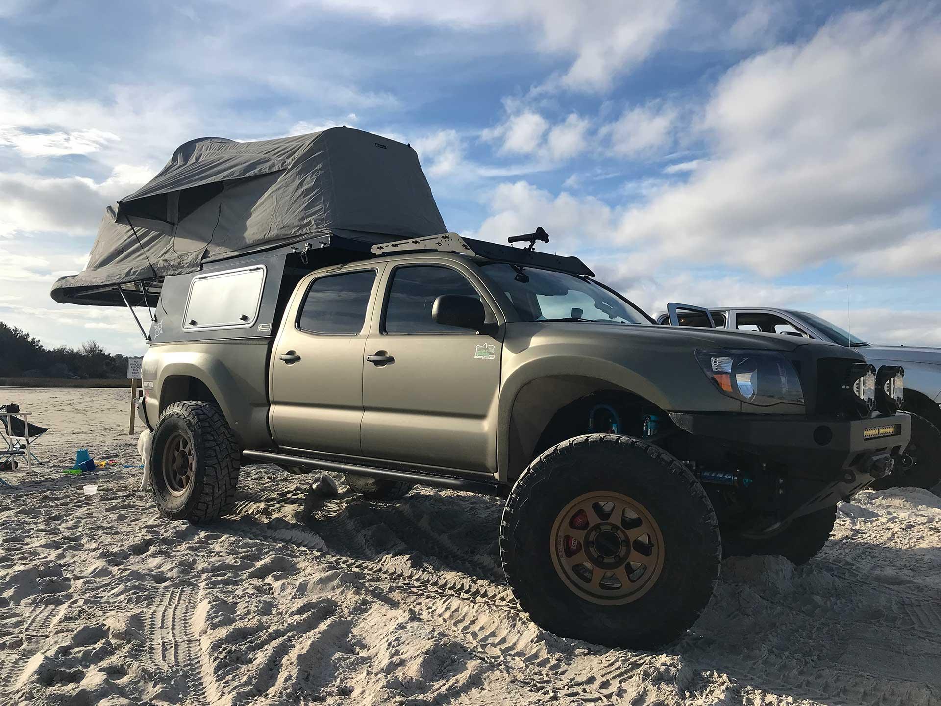 Toyota Tacoma overland truck with rooftop tent setup on sandy beach, ideal for expedition camping