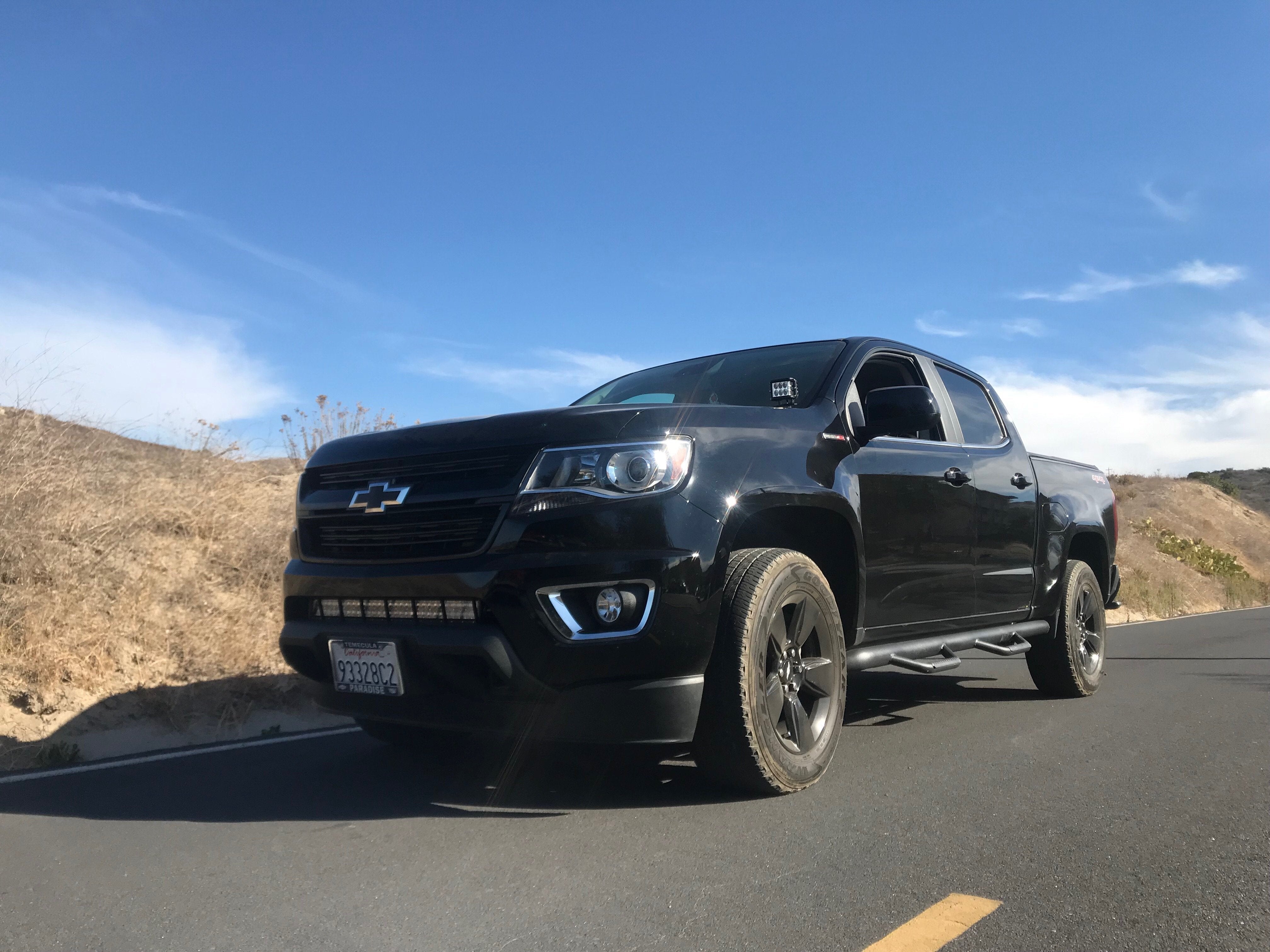 Black Chevrolet Colorado pickup truck with off-road accessories parked on scenic road