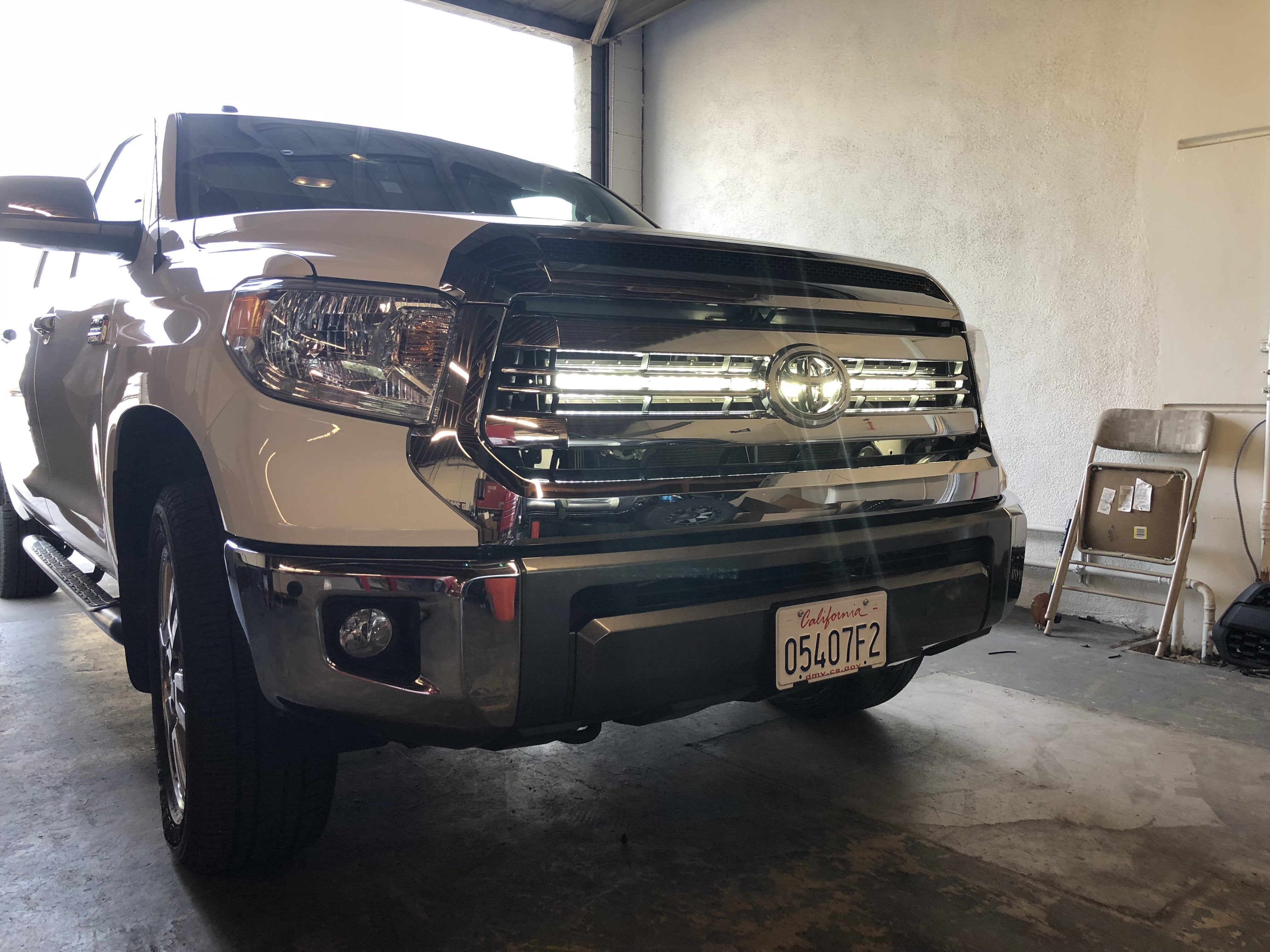 Front view of a white Toyota Tundra truck with aftermarket grille lights in a garage