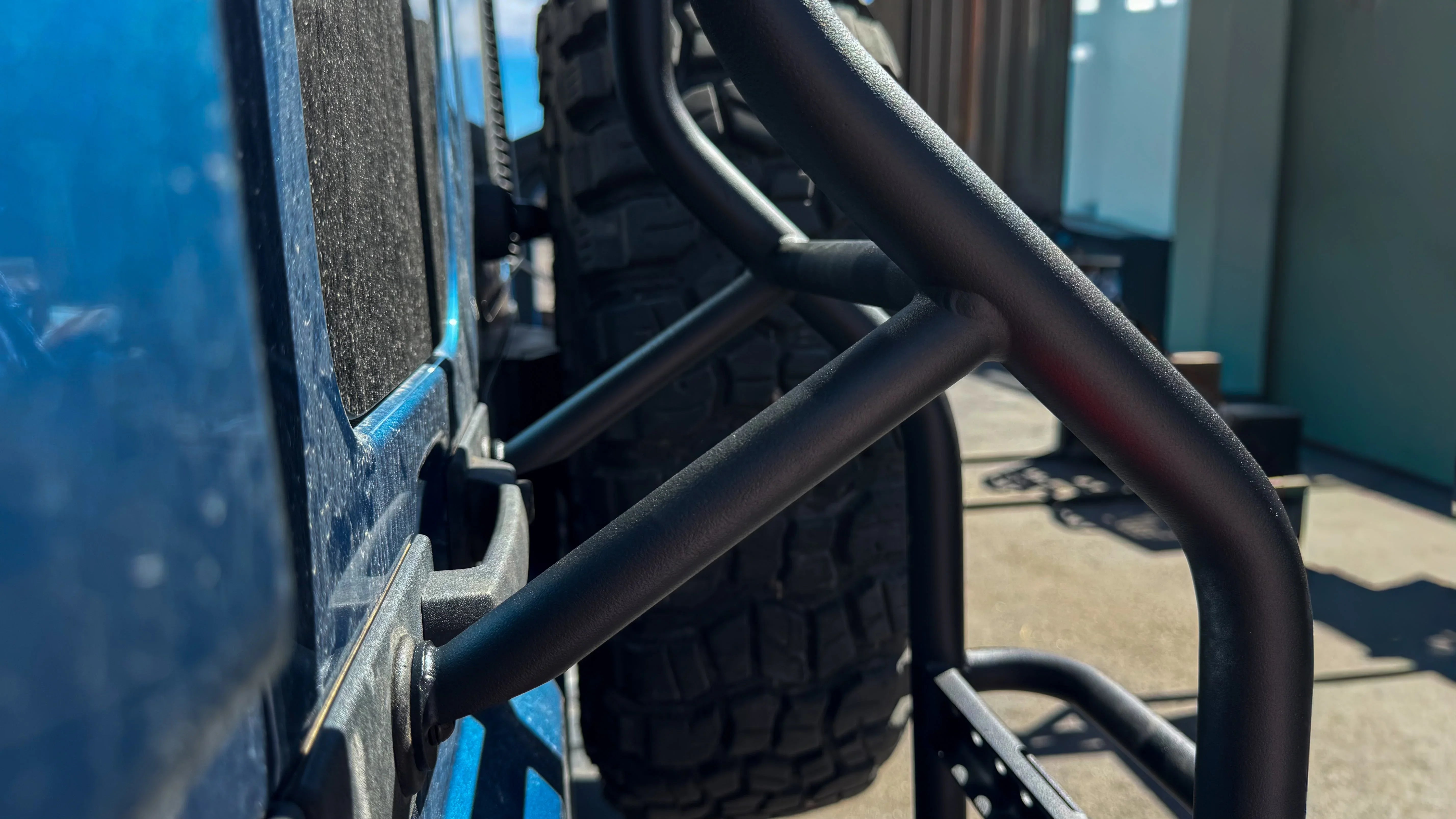 Close-up of rear ladder and body protection bar on an off-road vehicle with all-terrain tire.