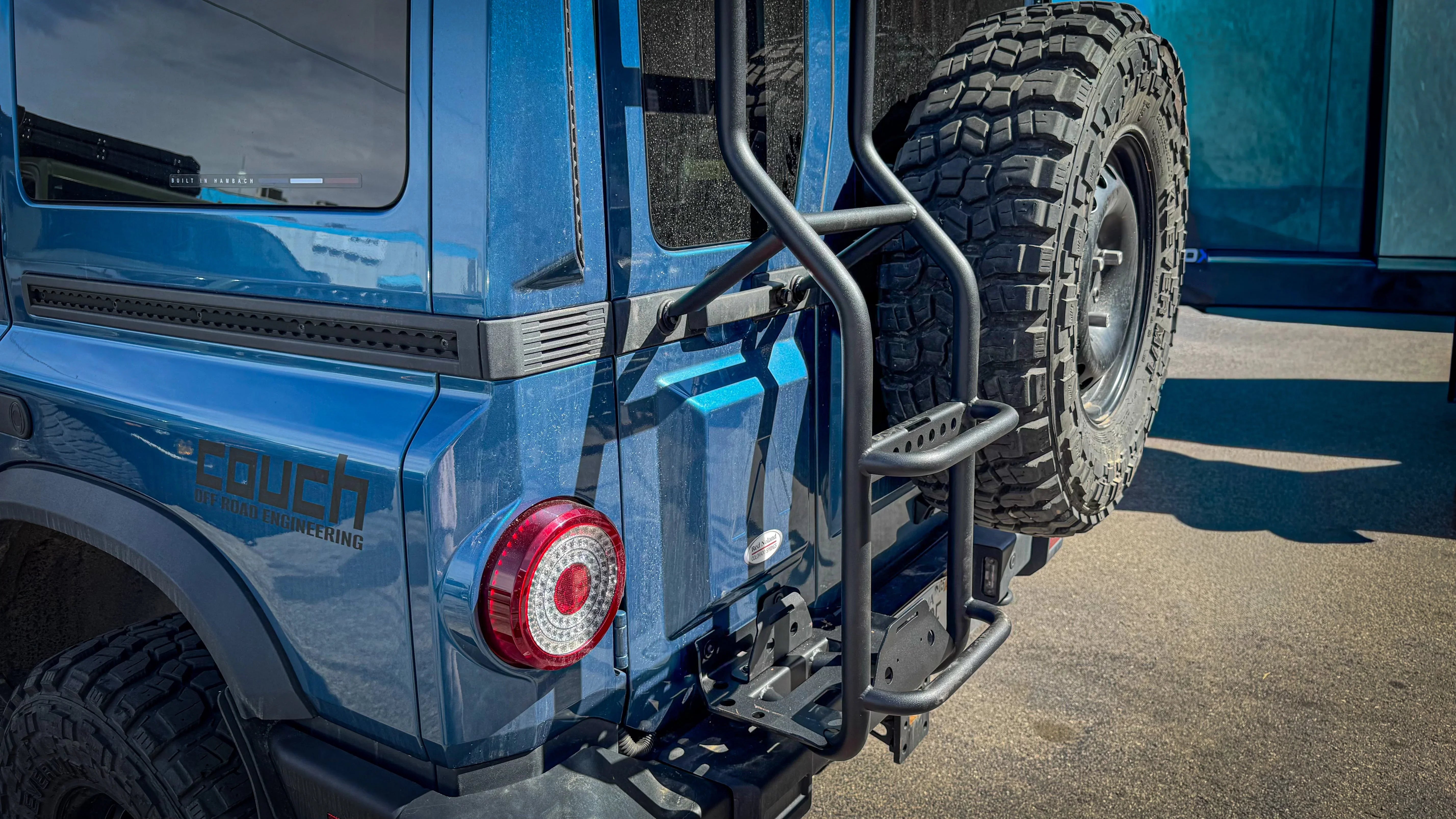 Rear ladder and roof top tent access on blue off-road vehicle with spare tire