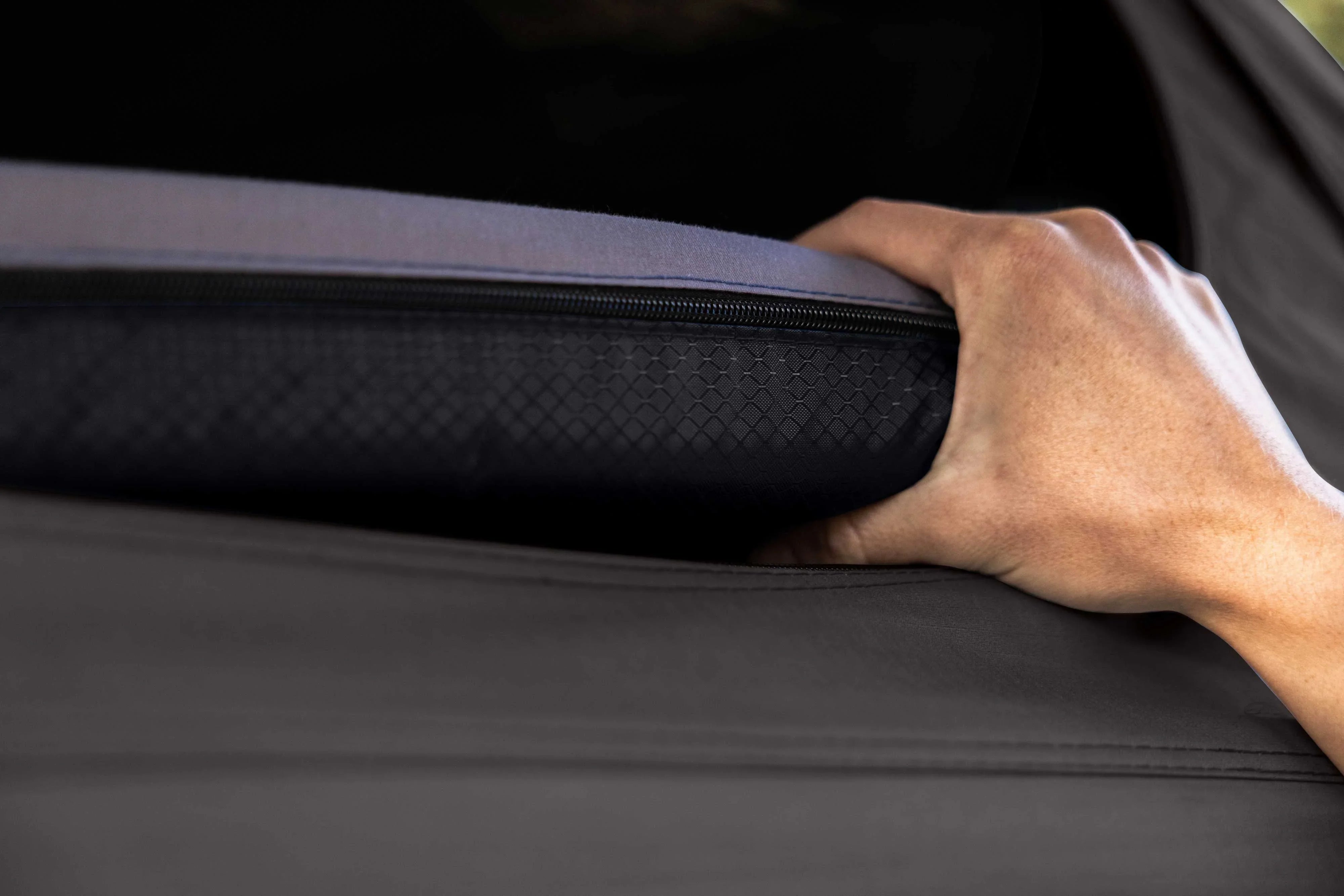 Closeup hand gripping a zippered camping mattress with textured cover for overlanding gear