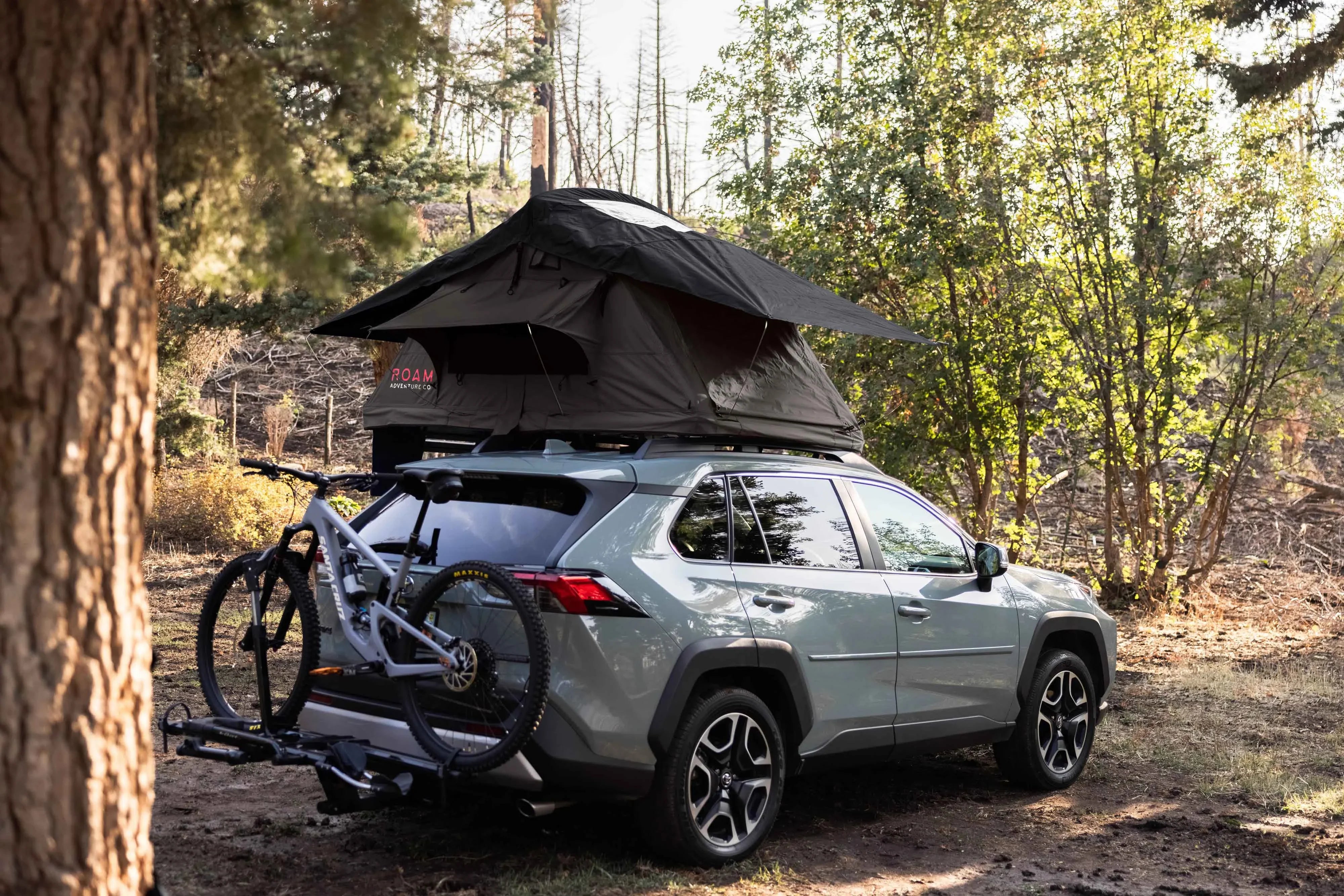 SUV with rooftop tent and mountain bike rack set up for overlanding in a forest campsite